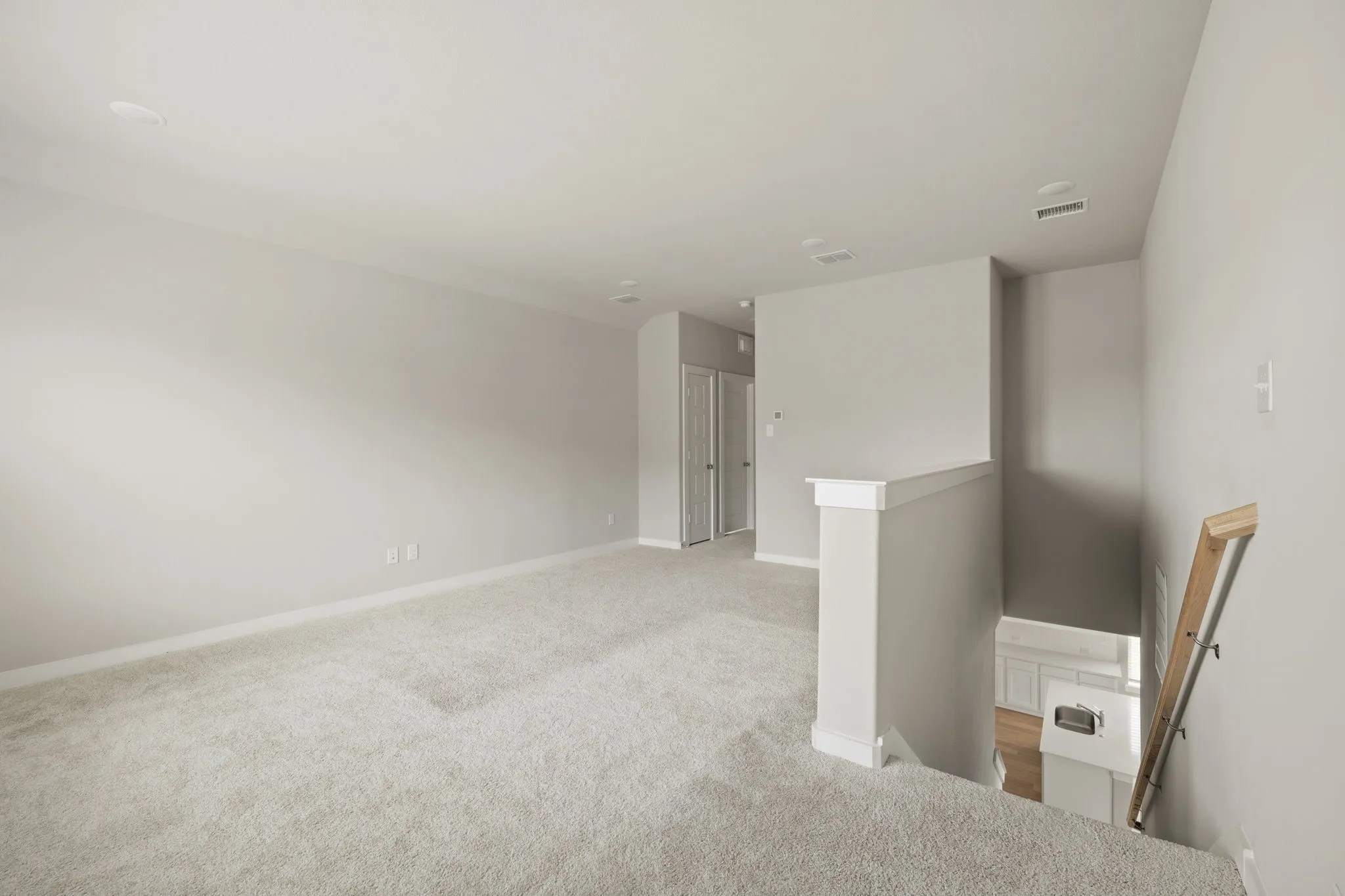 Spacious carpeted landing featuring recessed lighting, light gray wall paint, white baseboards, and a white balustrade with a wooden handrail