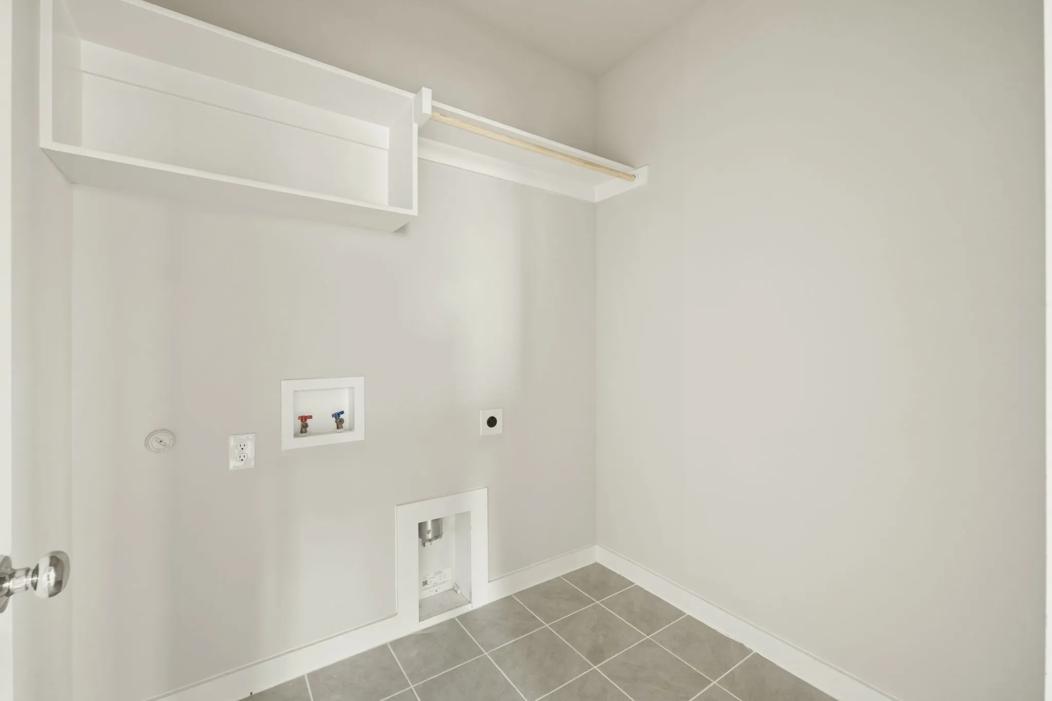 Dedicated utility space featuring a built-in shelf, clothing rod, and square tile flooring