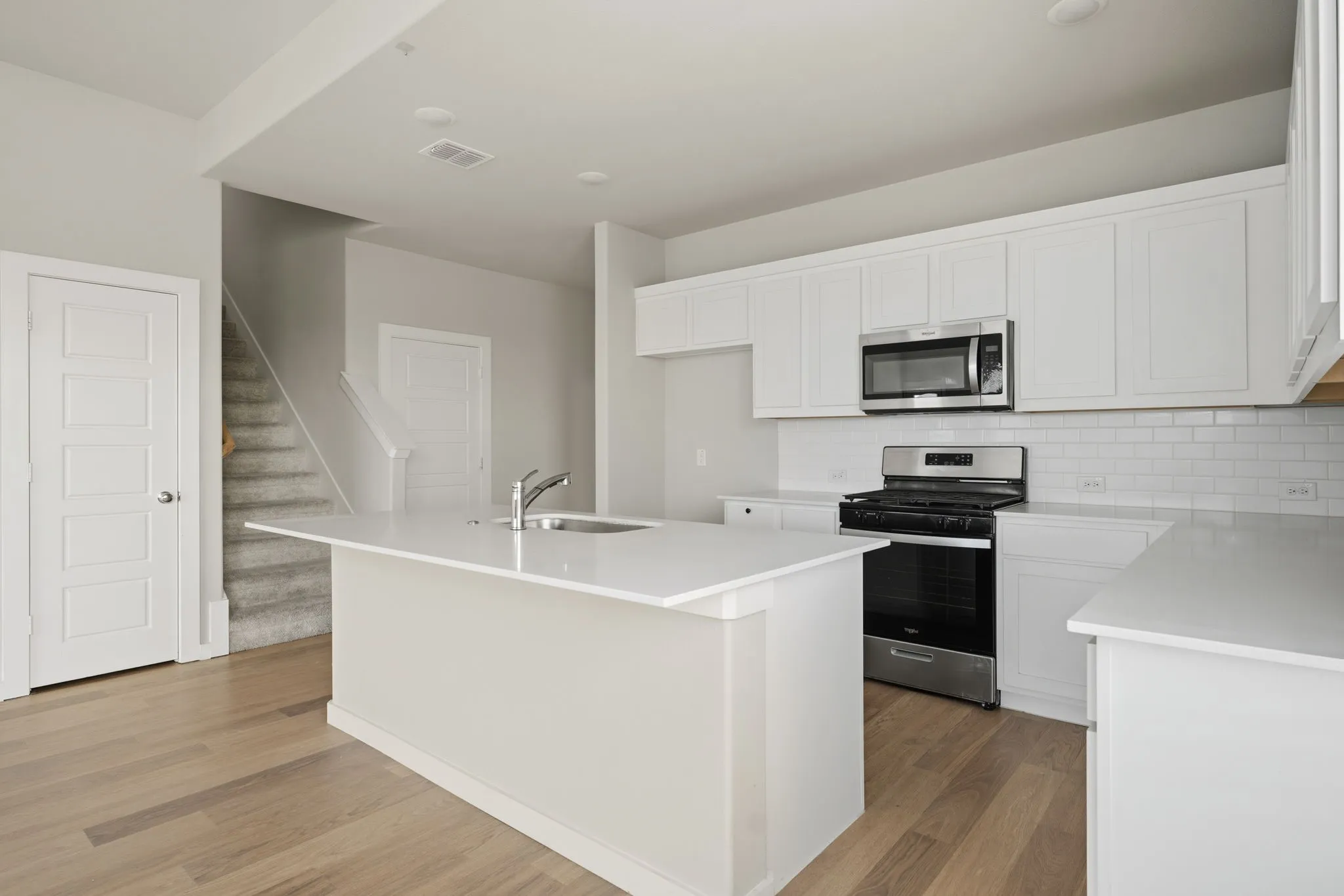Kitchen featuring a large island with an integrated sink, white shaker-style cabinetry, stainless steel appliances, white subway tile backsplash, and wood-finish flooring