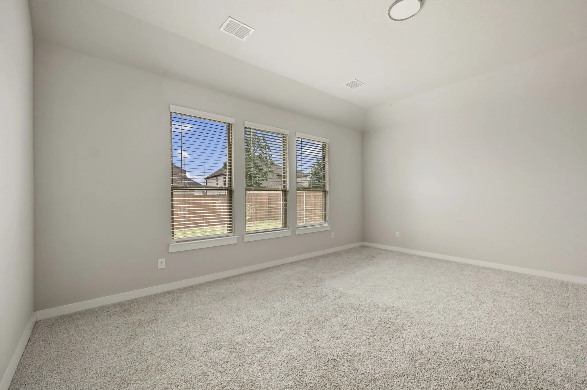 Neutral-toned room with three windows featuring blinds, light gray wall paint, and light-colored carpeting