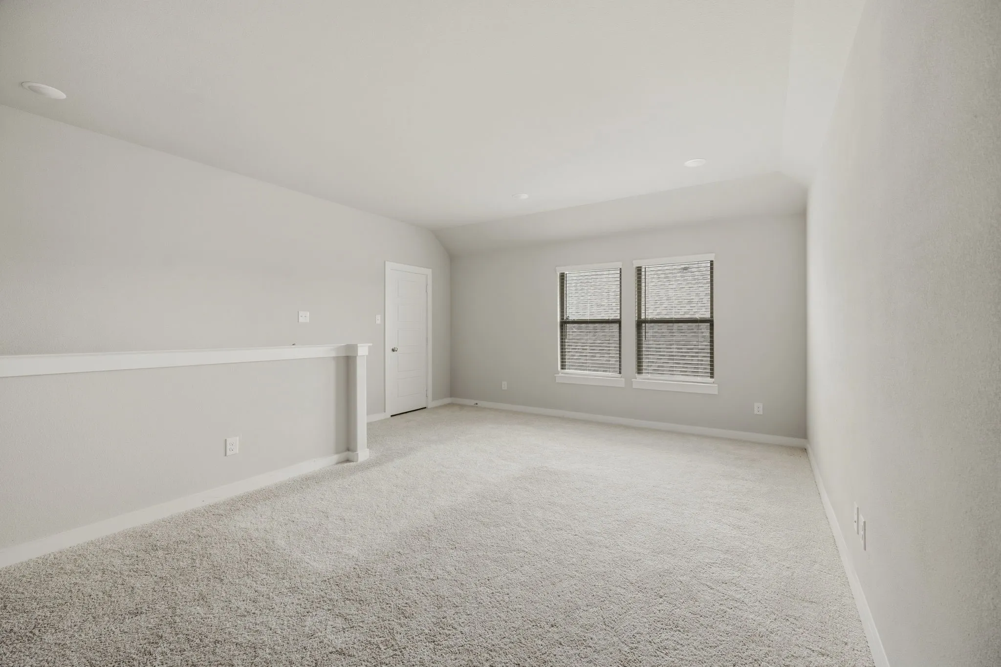 Spacious carpeted room featuring light gray walls, two windows with blinds, a white door, and recessed lighting