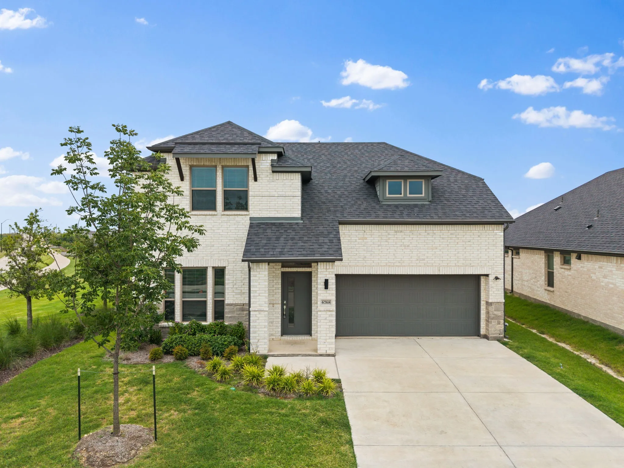 Contemporary two-story residence featuring light brick masonry, a dark shingled roof, and a two-car garage with a dark door