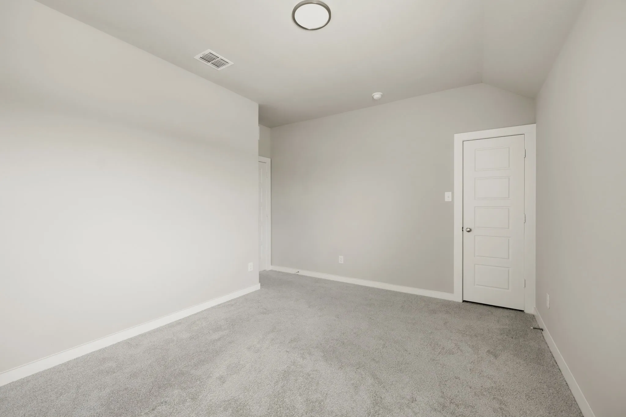 Carpeted room with vaulted ceiling and a five-panel interior door