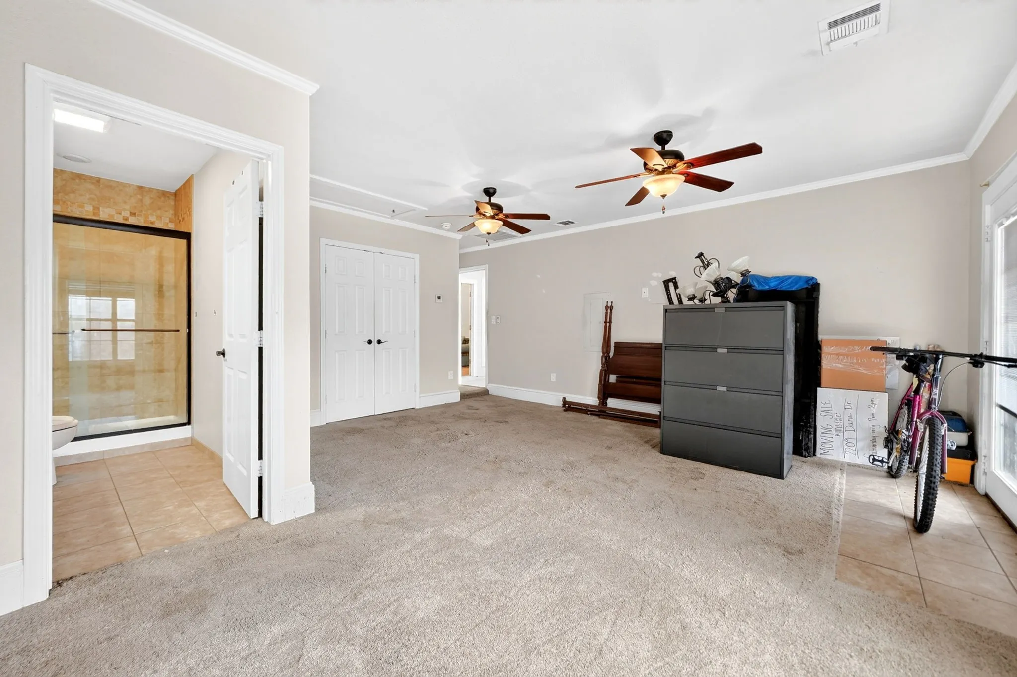 Spacious room featuring neutral carpeting, crown molding, and two ceiling fans with integrated lighting