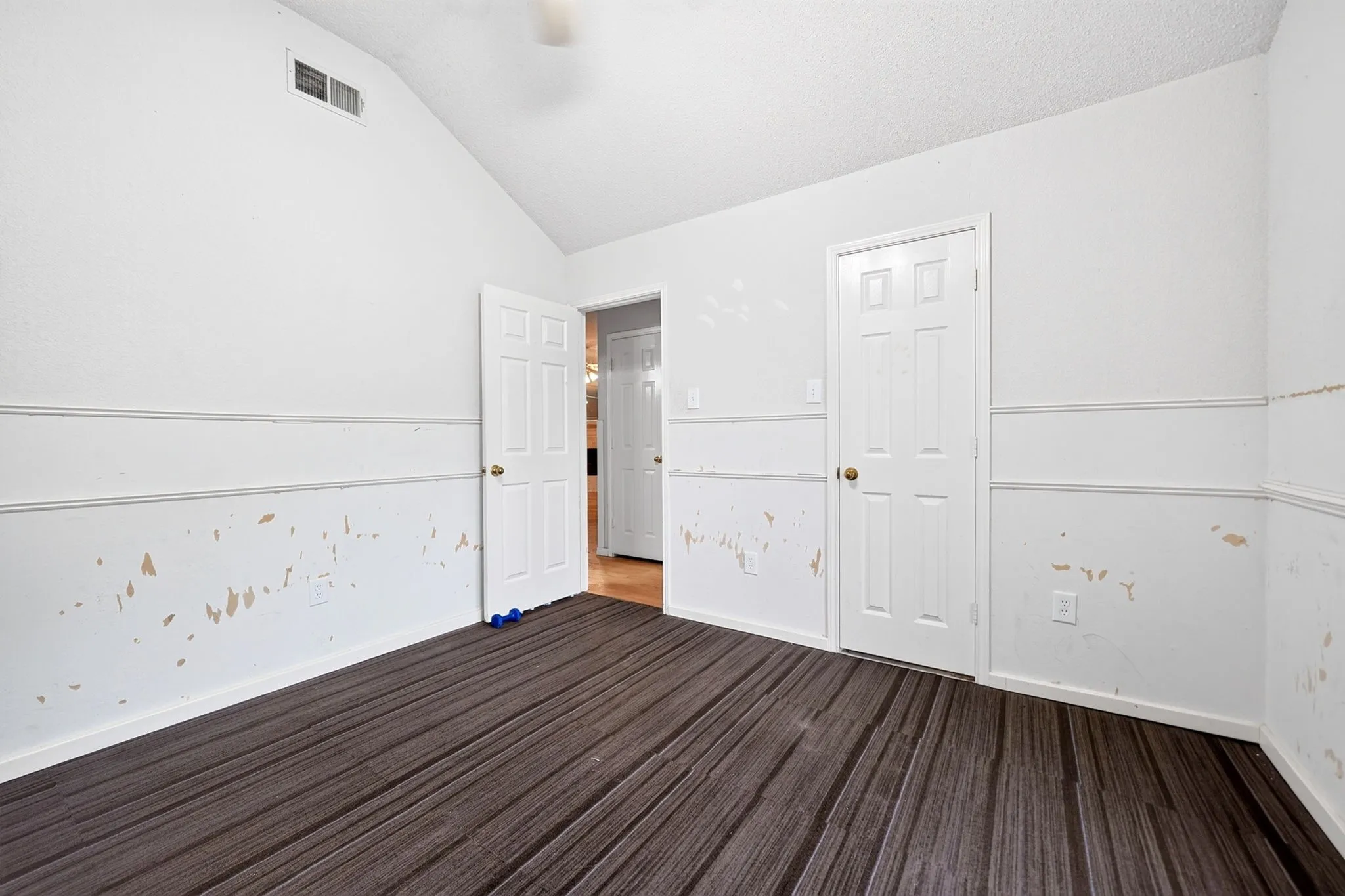 Vaulted ceiling room featuring wood-finish flooring, white paneled doors, and wainscoting