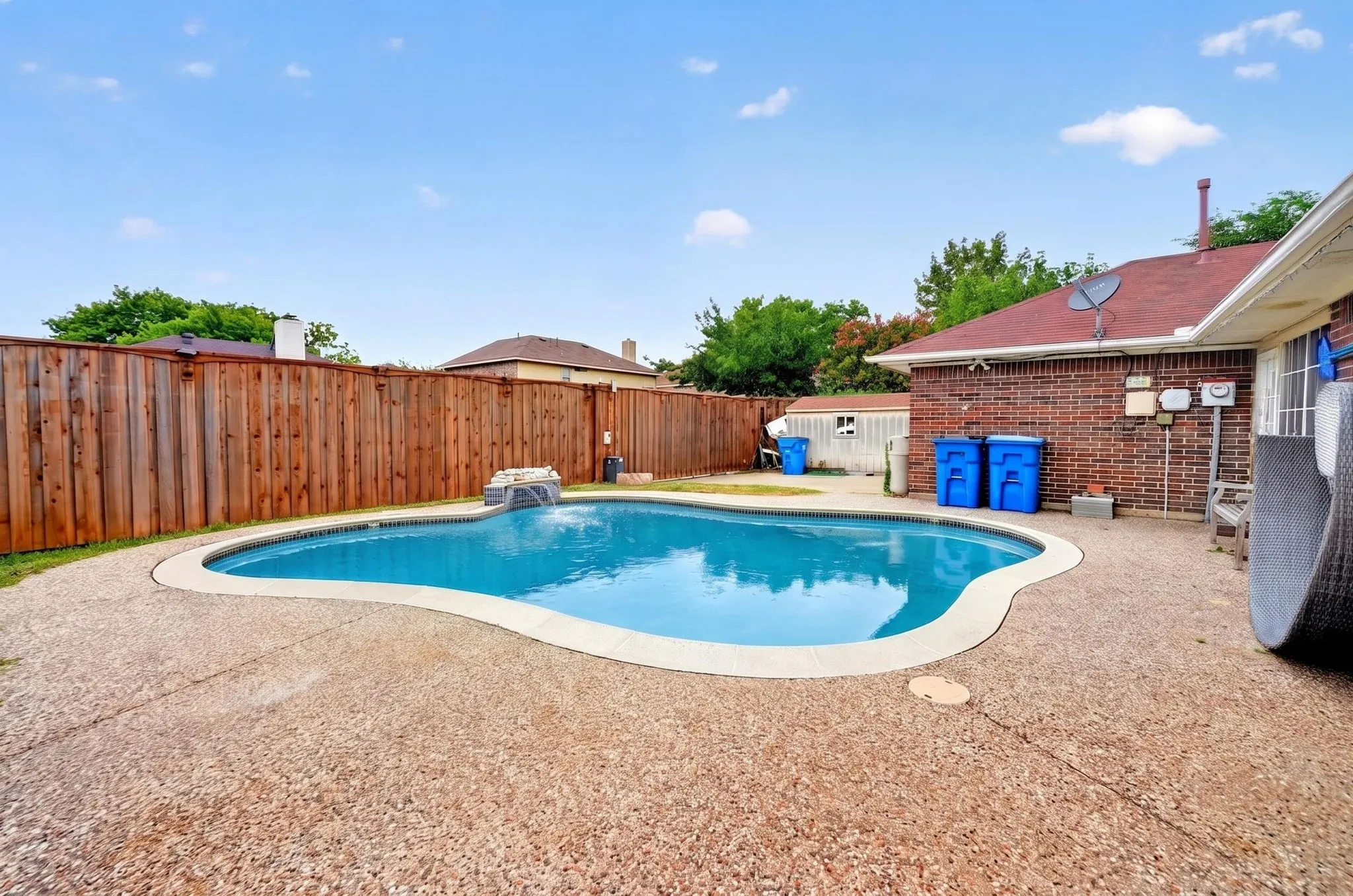 Freestyle swimming pool with a waterfall feature, surrounded by an exposed aggregate concrete patio