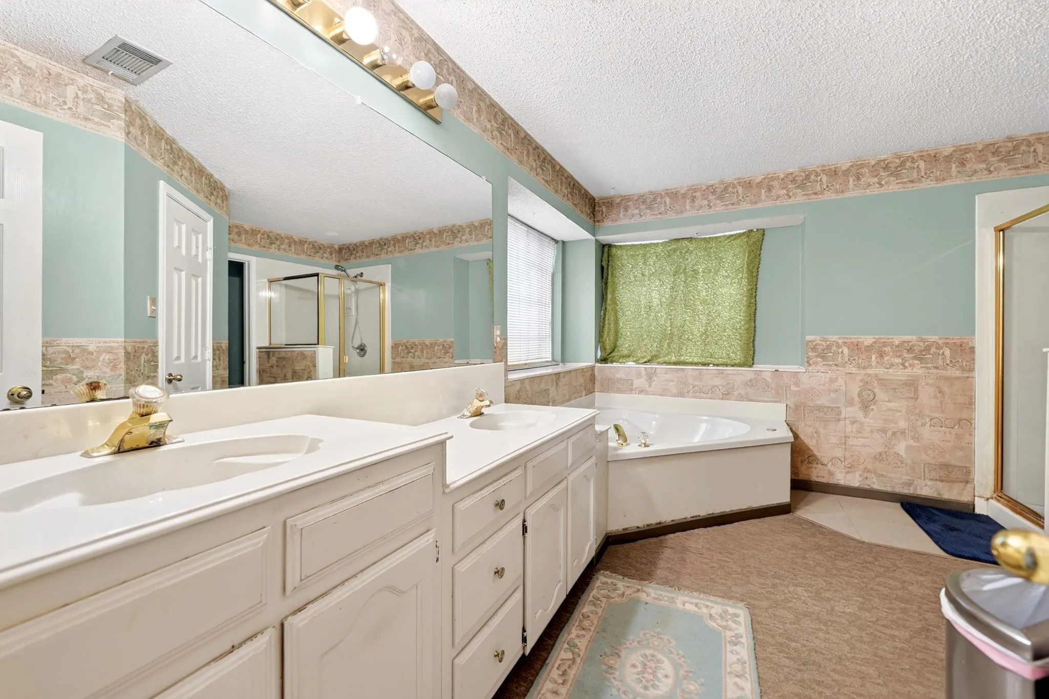Bathroom featuring a double vanity with built-in sinks, an expansive wall mirror, a corner built-in bathtub, and a separate glass-enclosed shower