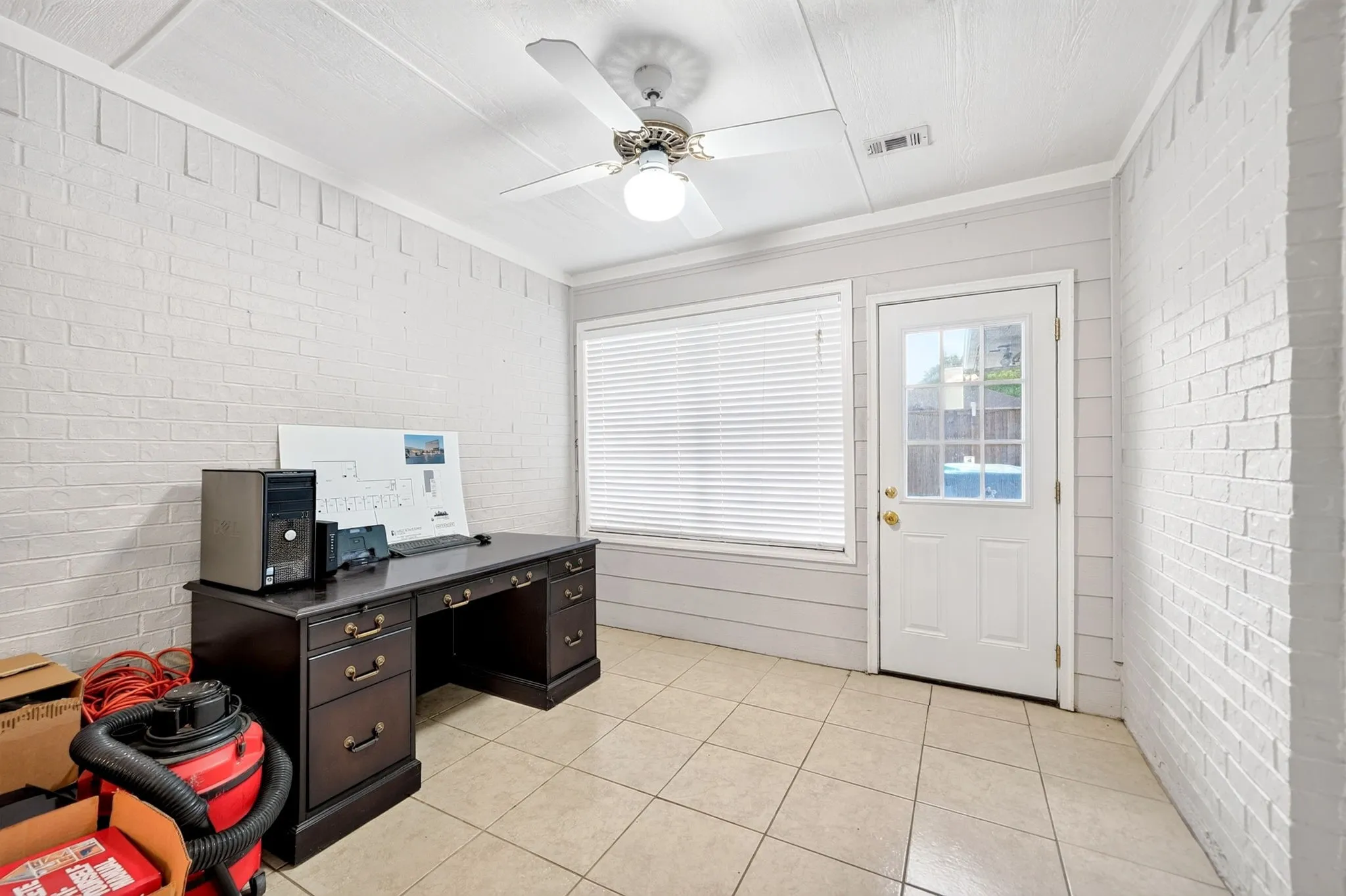 Spacious room featuring white painted brick walls, tile flooring, and a ceiling fan