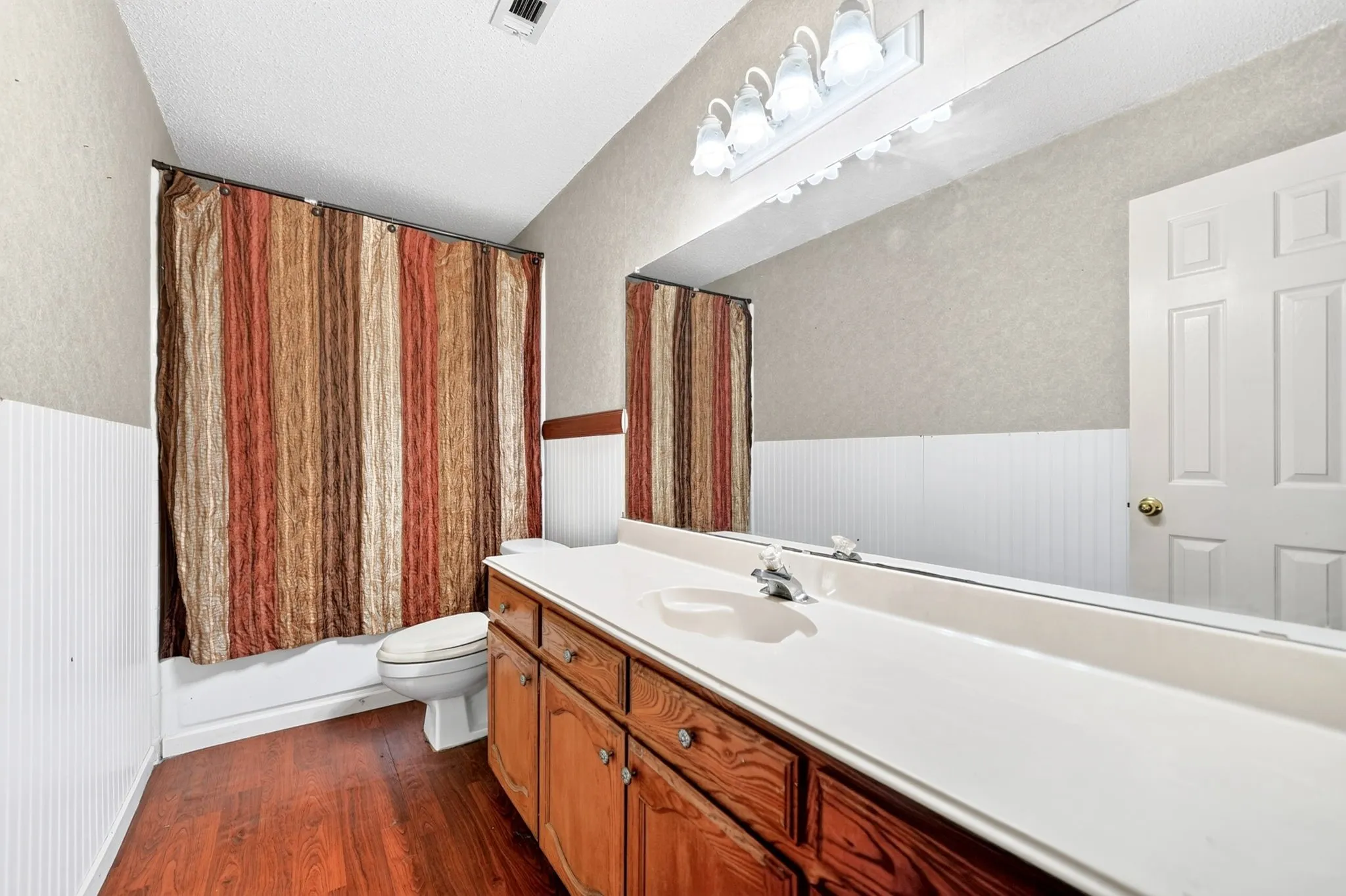 Bathroom featuring a wood-finish floor, wood vanity with integrated countertop and sink, and a full-width mirror