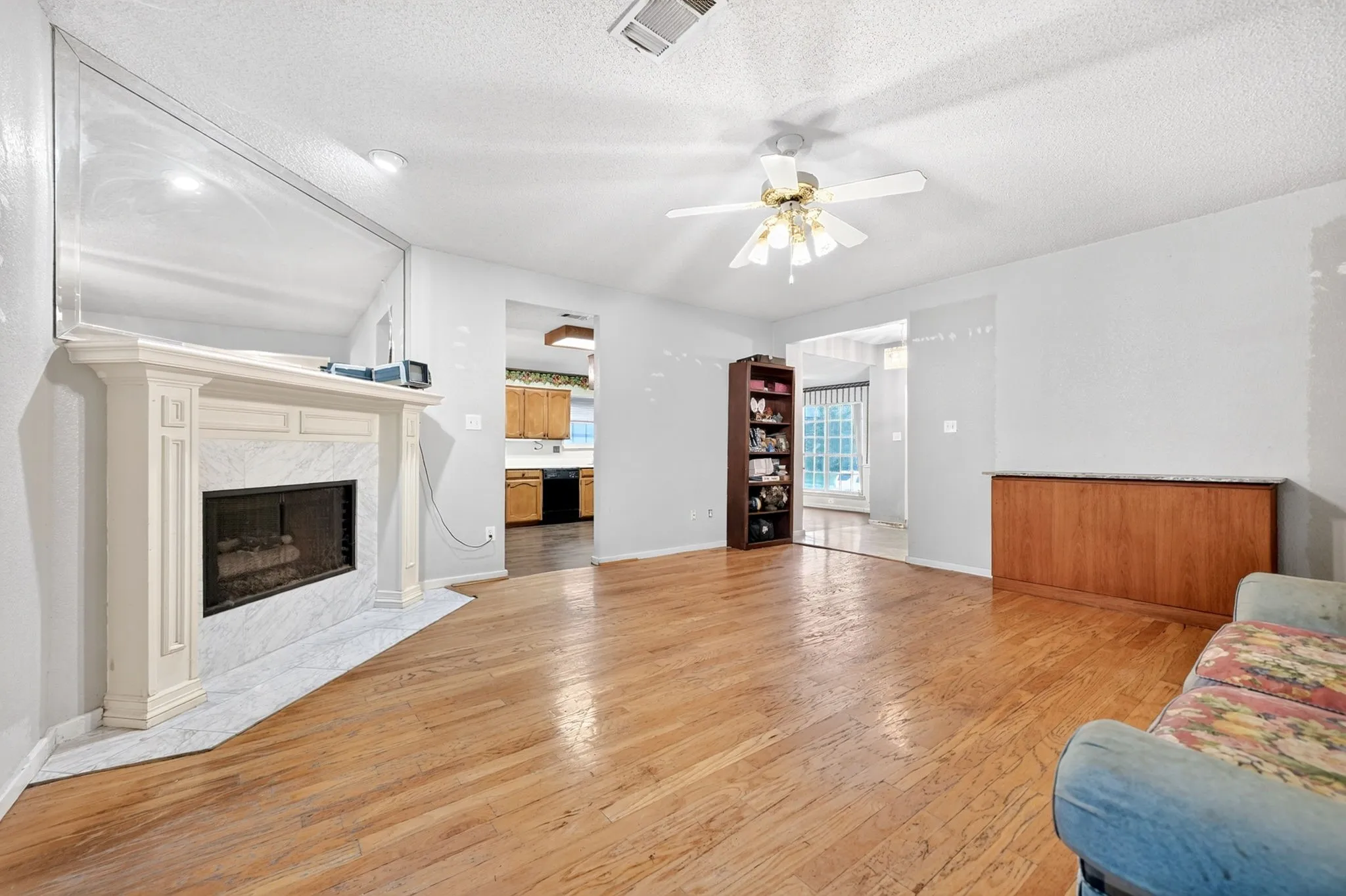 Living area with wood-finish flooring, a white mantel fireplace featuring a marble surround and hearth, and a ceiling fan