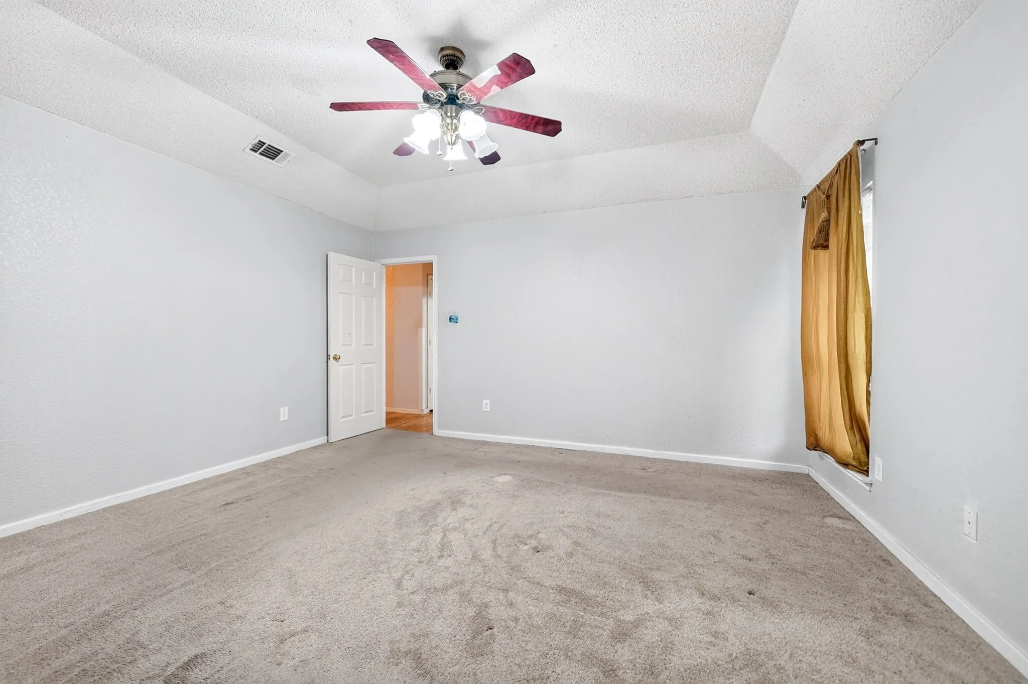 Spacious room featuring a tray ceiling with a ceiling fan, light gray wall paint, and gray carpeted flooring