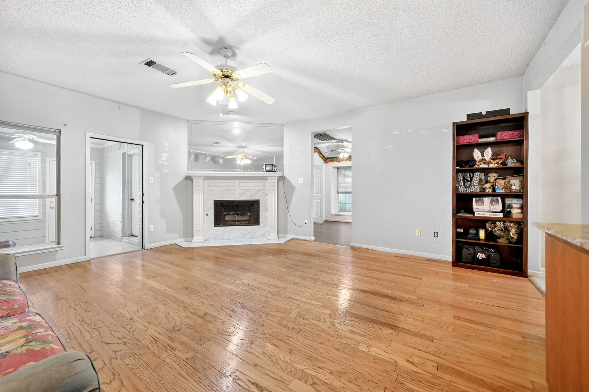 Living area featuring wood-finish flooring, a white fireplace with a mirrored surround, and a ceiling fan