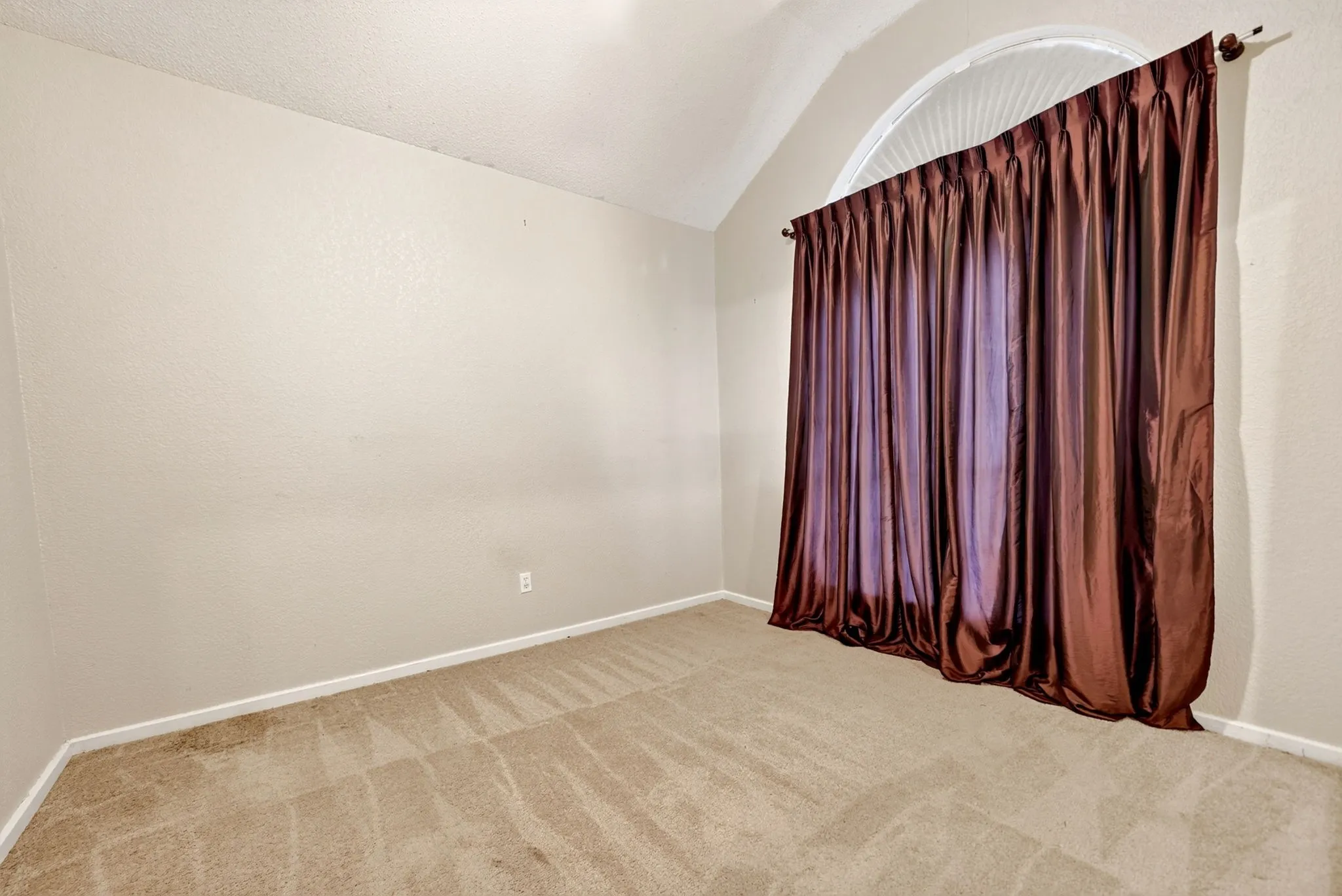 Vaulted ceiling room featuring a large arched window, neutral wall paint, and plush carpet flooring