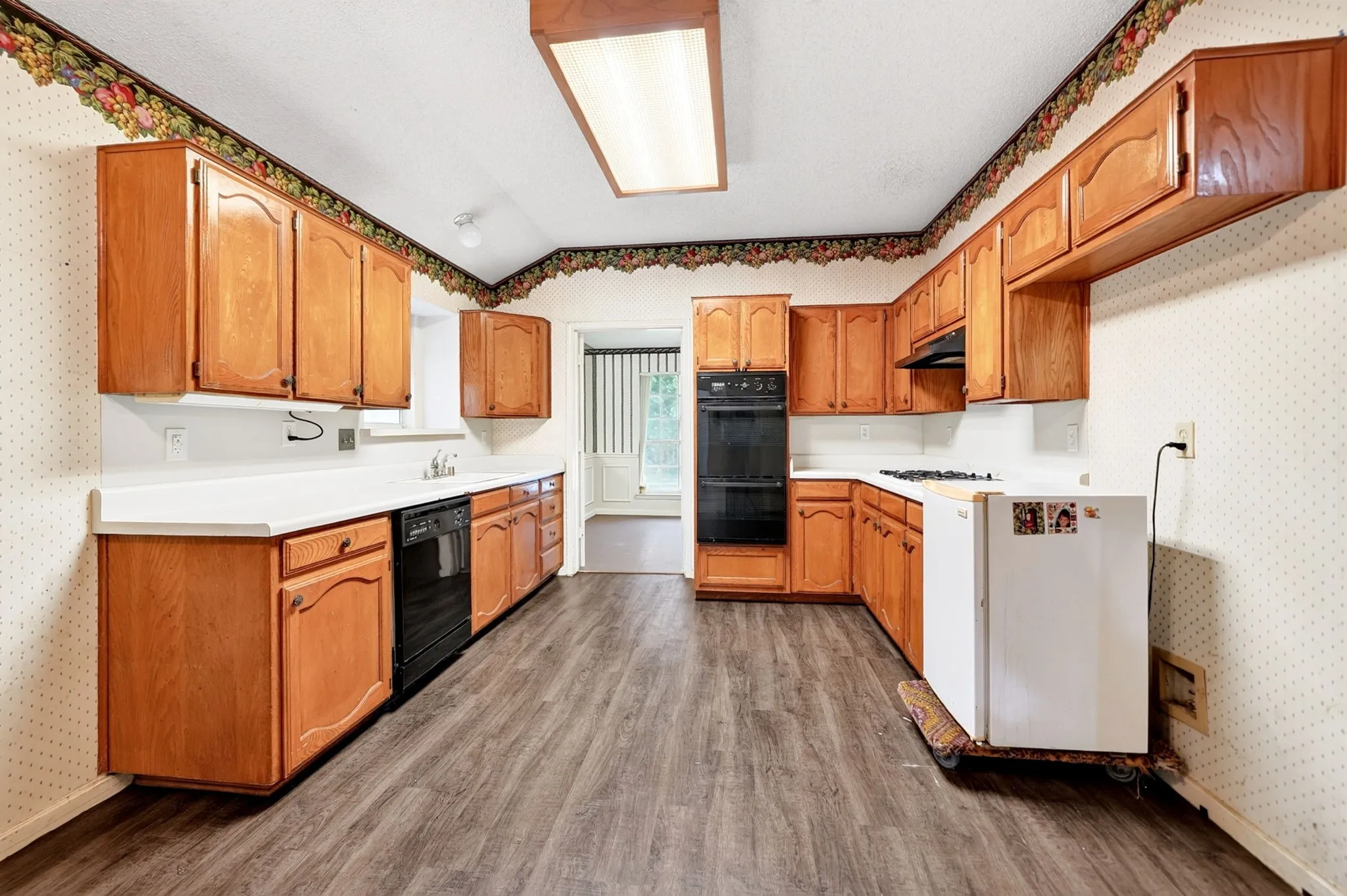Spacious kitchen featuring extensive wood cabinetry, light countertops, integrated wall oven, cooktop, and wood-finish flooring