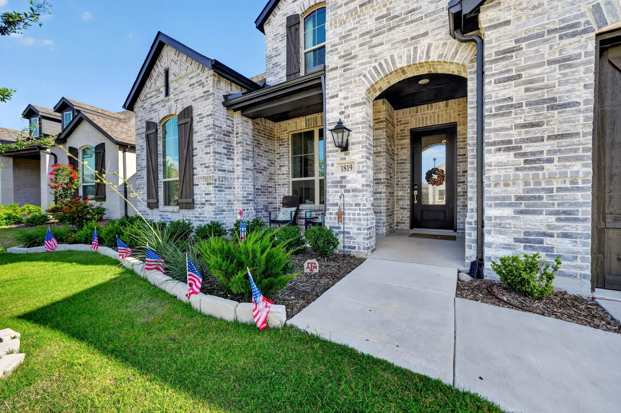 Light brick exterior featuring dark trim, arched entryway, and dark wood shutters
