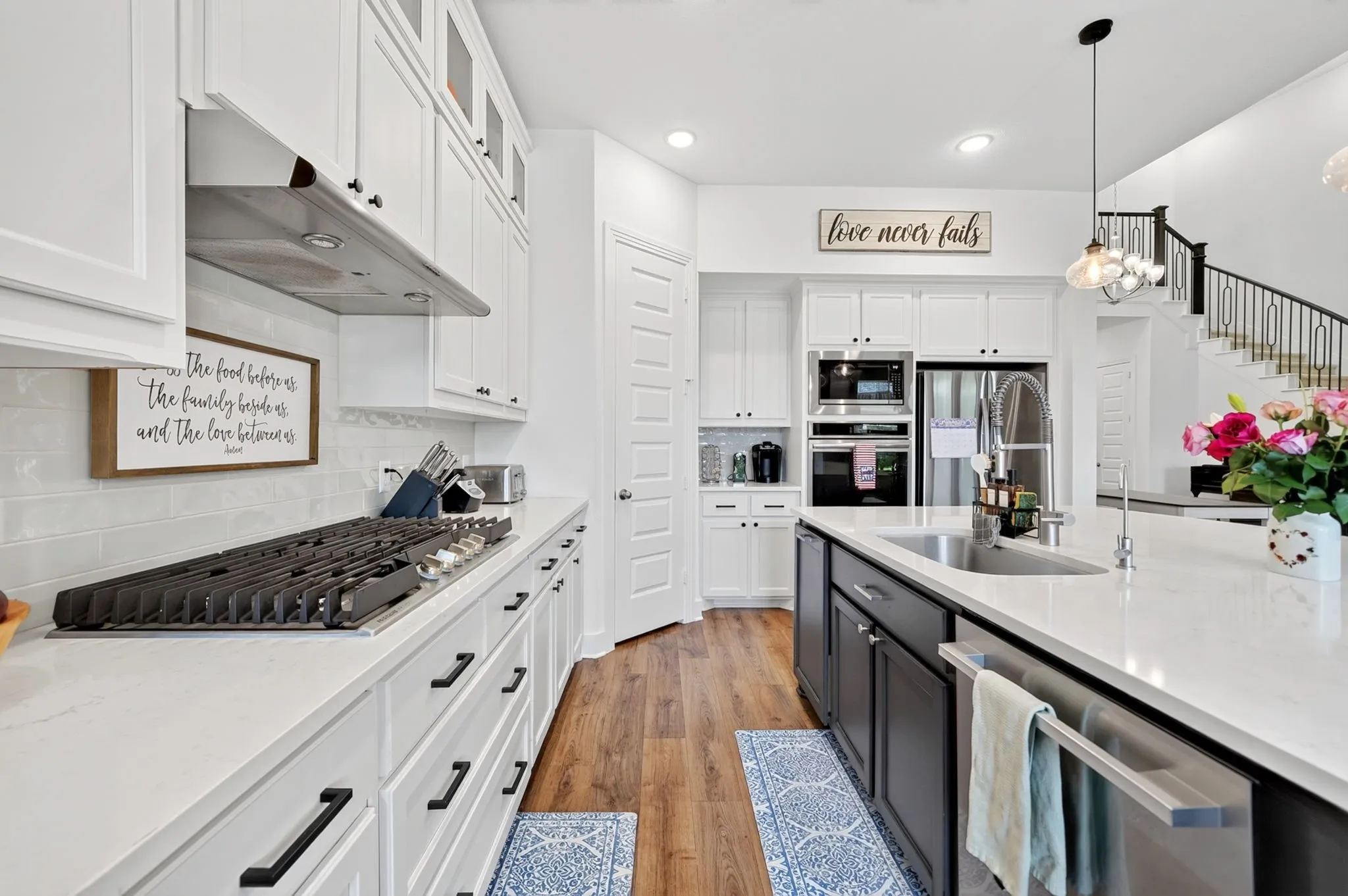 Gourmet kitchen featuring a gas range, built-in double ovens, stainless steel appliances, white cabinetry with black hardware, and wood-finish flooring