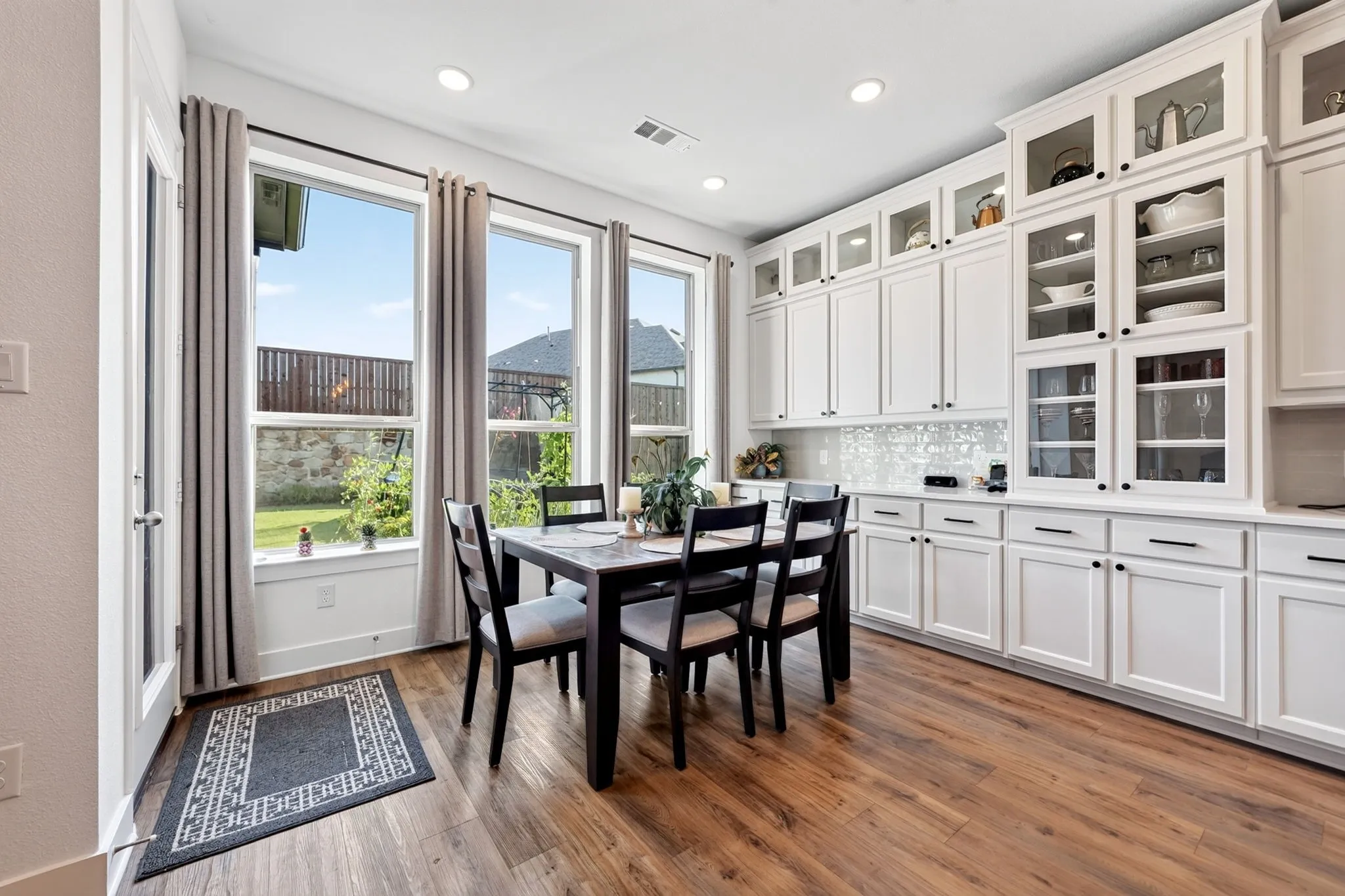 Open-concept dining area featuring wood-finish flooring, extensive built-in white cabinetry with glass-front uppers, and recessed lighting