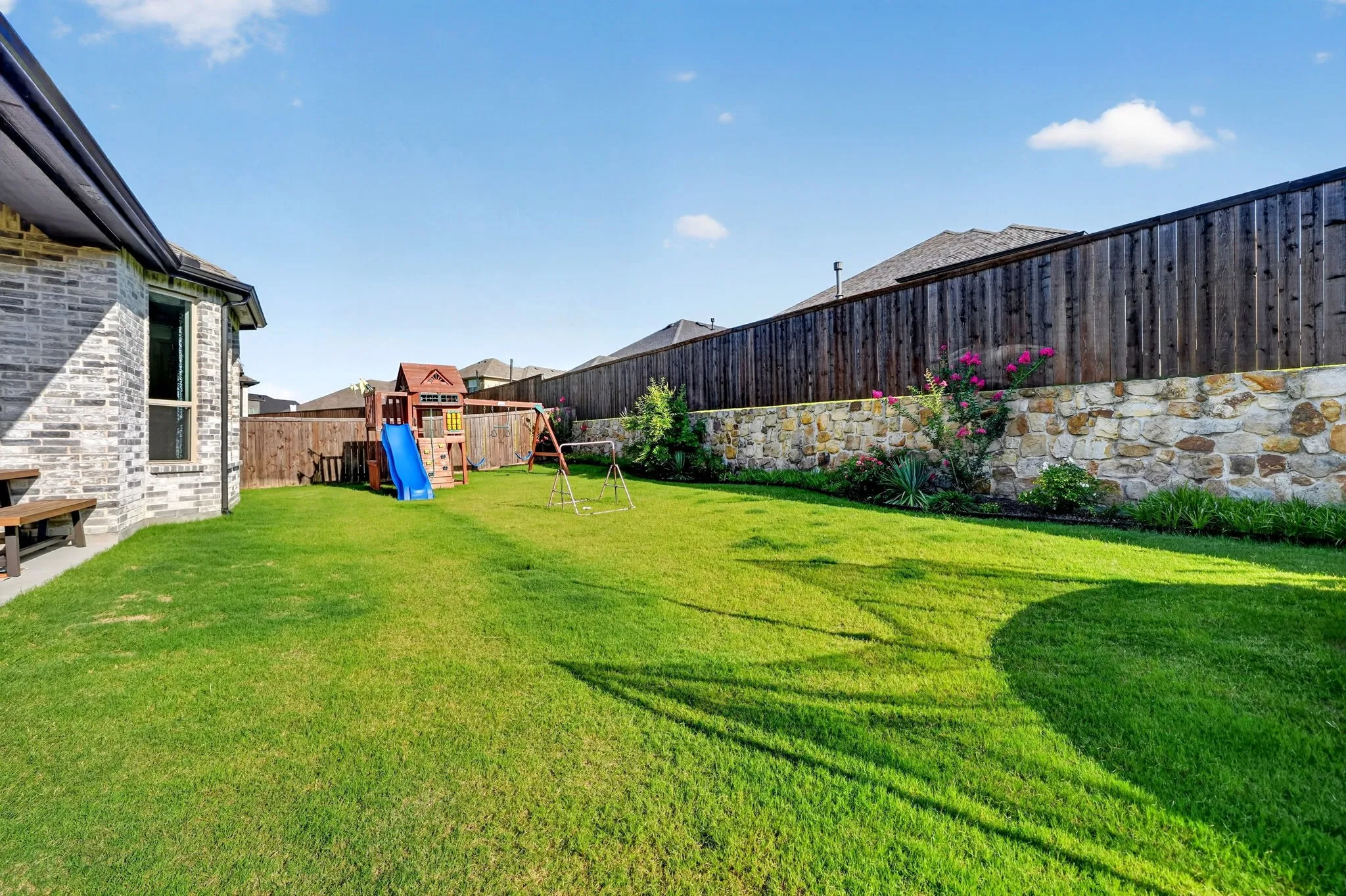 Expansive green lawn with a natural stone retaining wall and a privacy fence