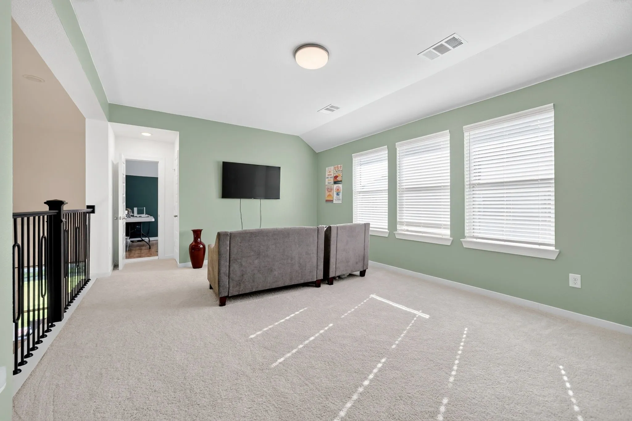 Open loft area featuring three windows with blinds, a wall-mounted television, and light-colored carpet flooring