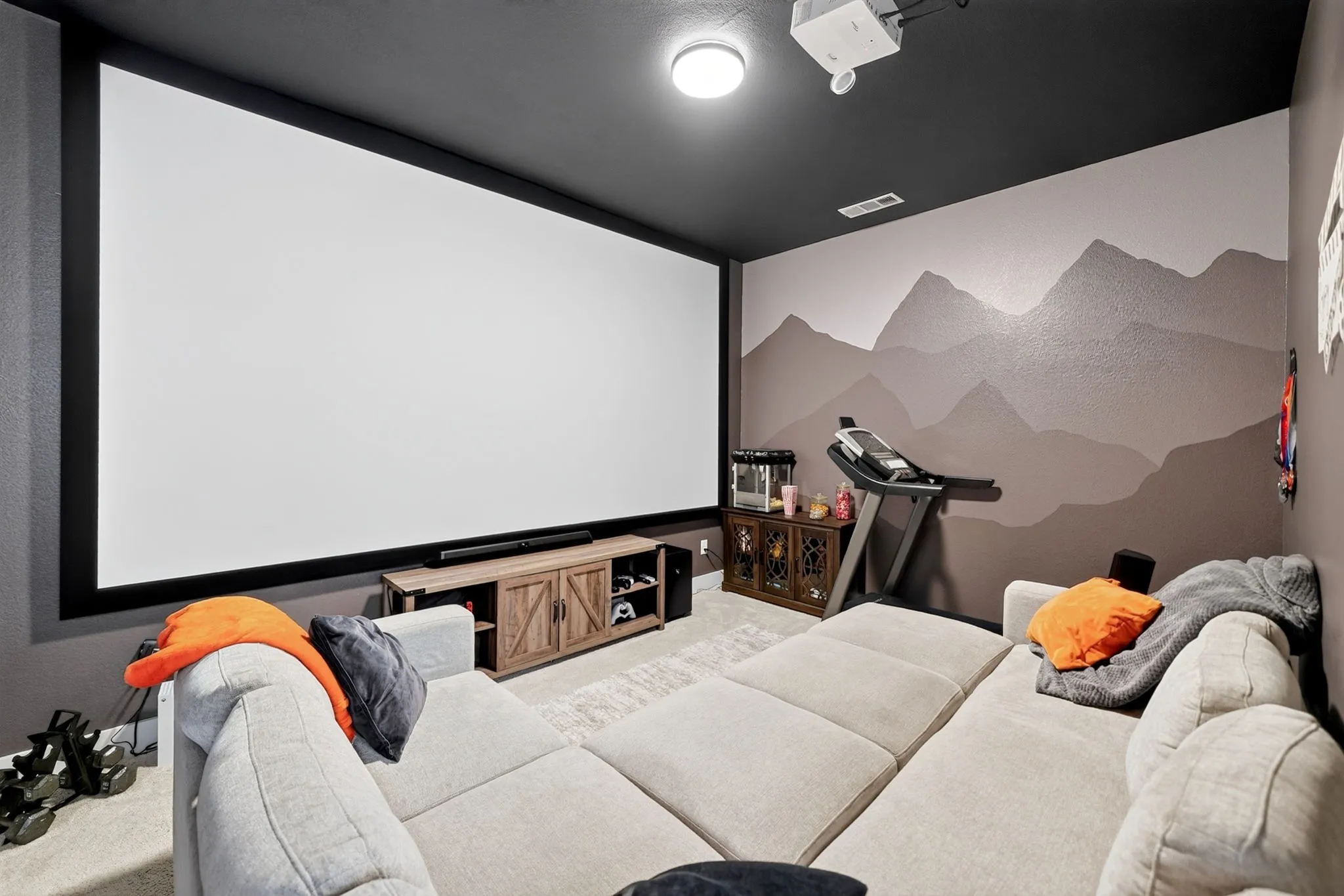 Dedicated media room featuring an expansive projection screen, wall-mounted projector, and a custom mountain mural