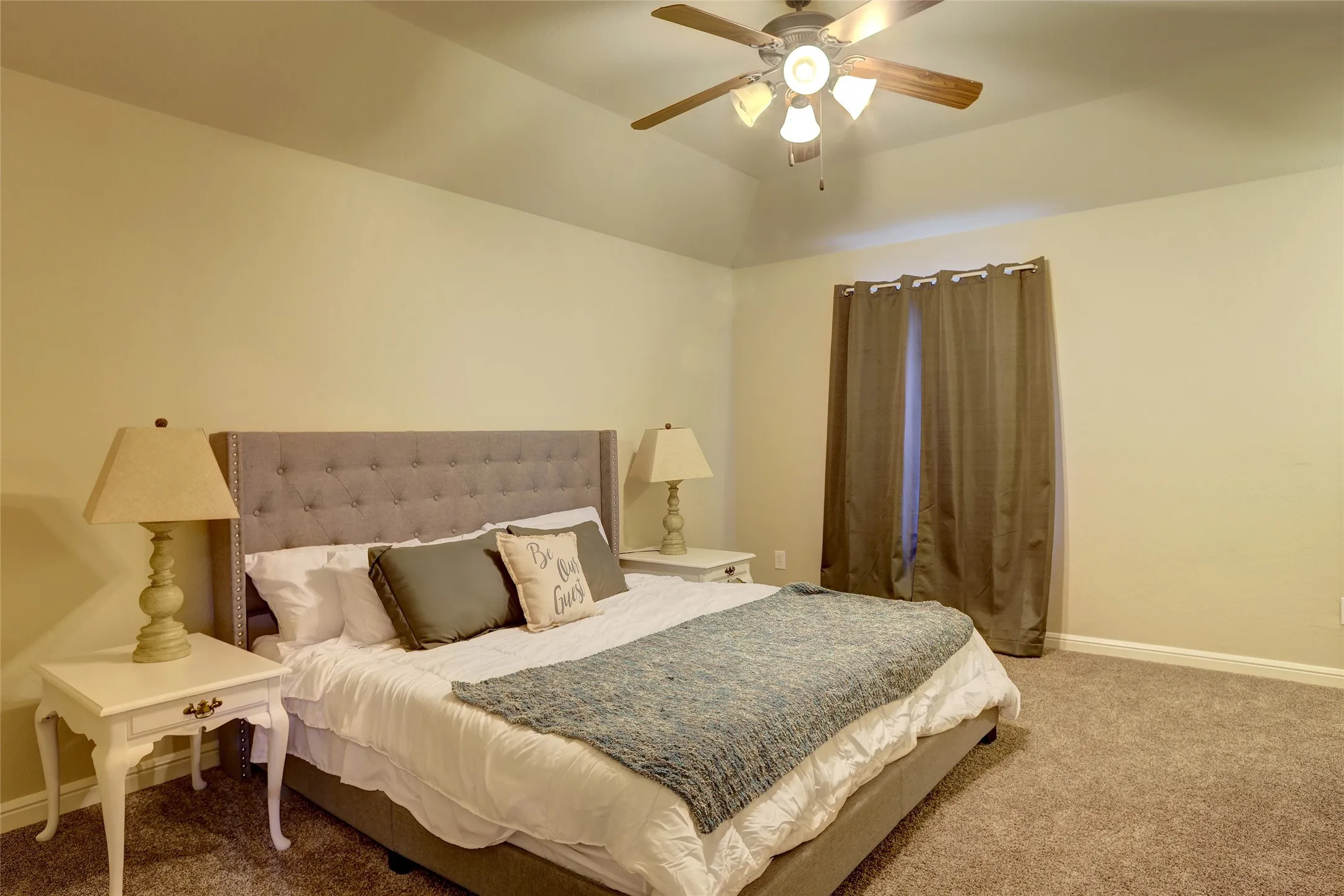 Carpeted bedroom featuring a tray ceiling, ceiling fan with integrated lighting, and a window with curtain rod