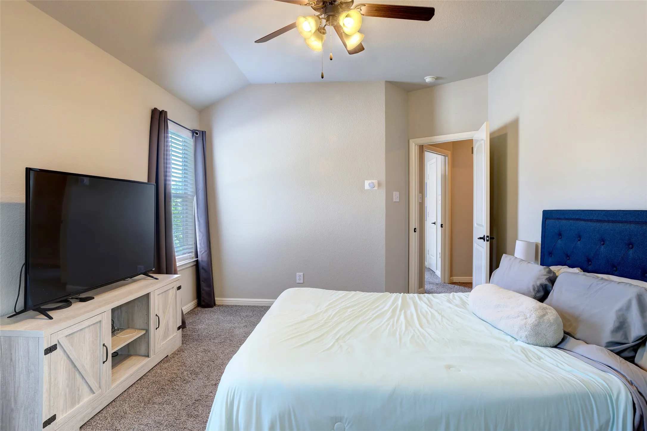 Carpeted bedroom featuring a vaulted ceiling and a ceiling fan