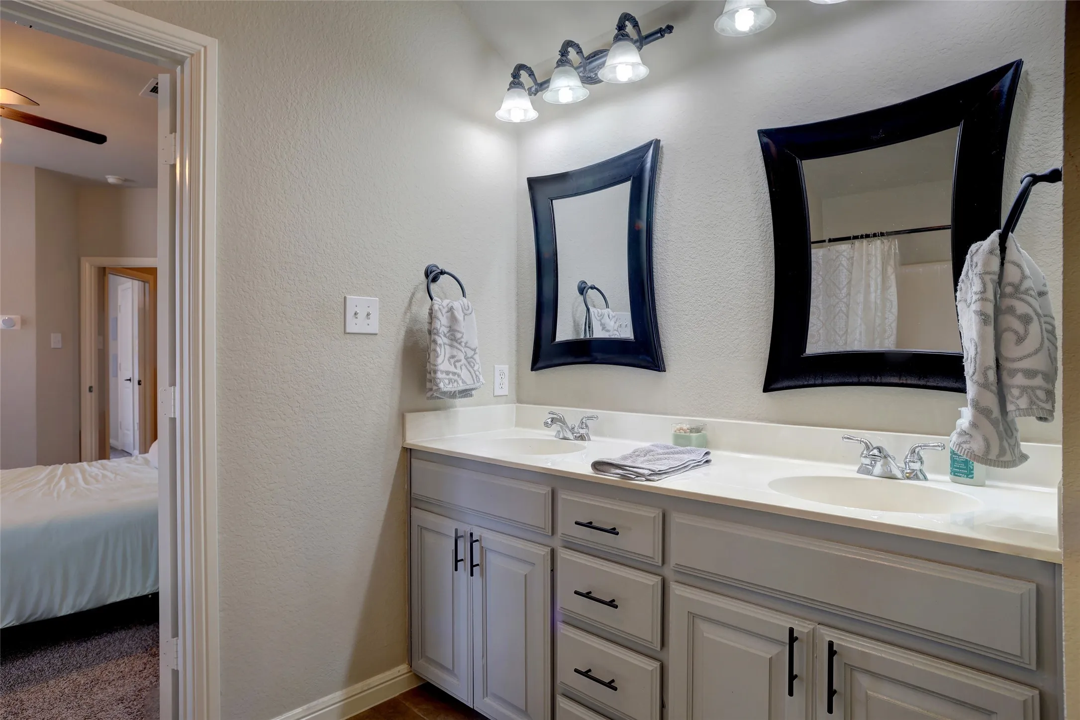 Dual vanity featuring light-toned cabinetry with black hardware, two integrated sinks, and individual framed mirrors