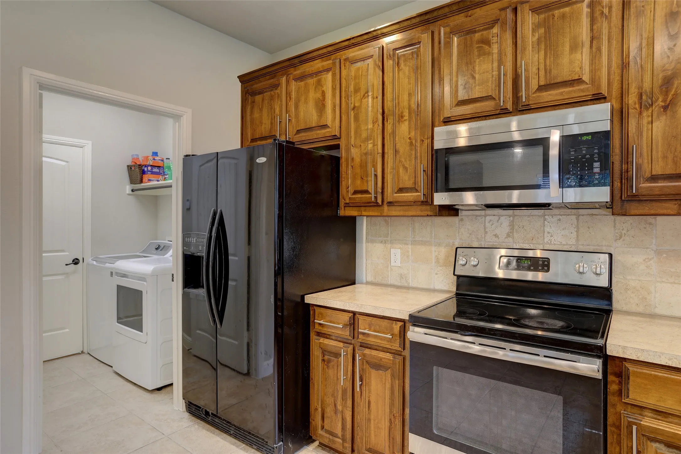 Kitchen featuring wood cabinetry, stainless steel microwave, black electric range, and light-toned tile backsplash