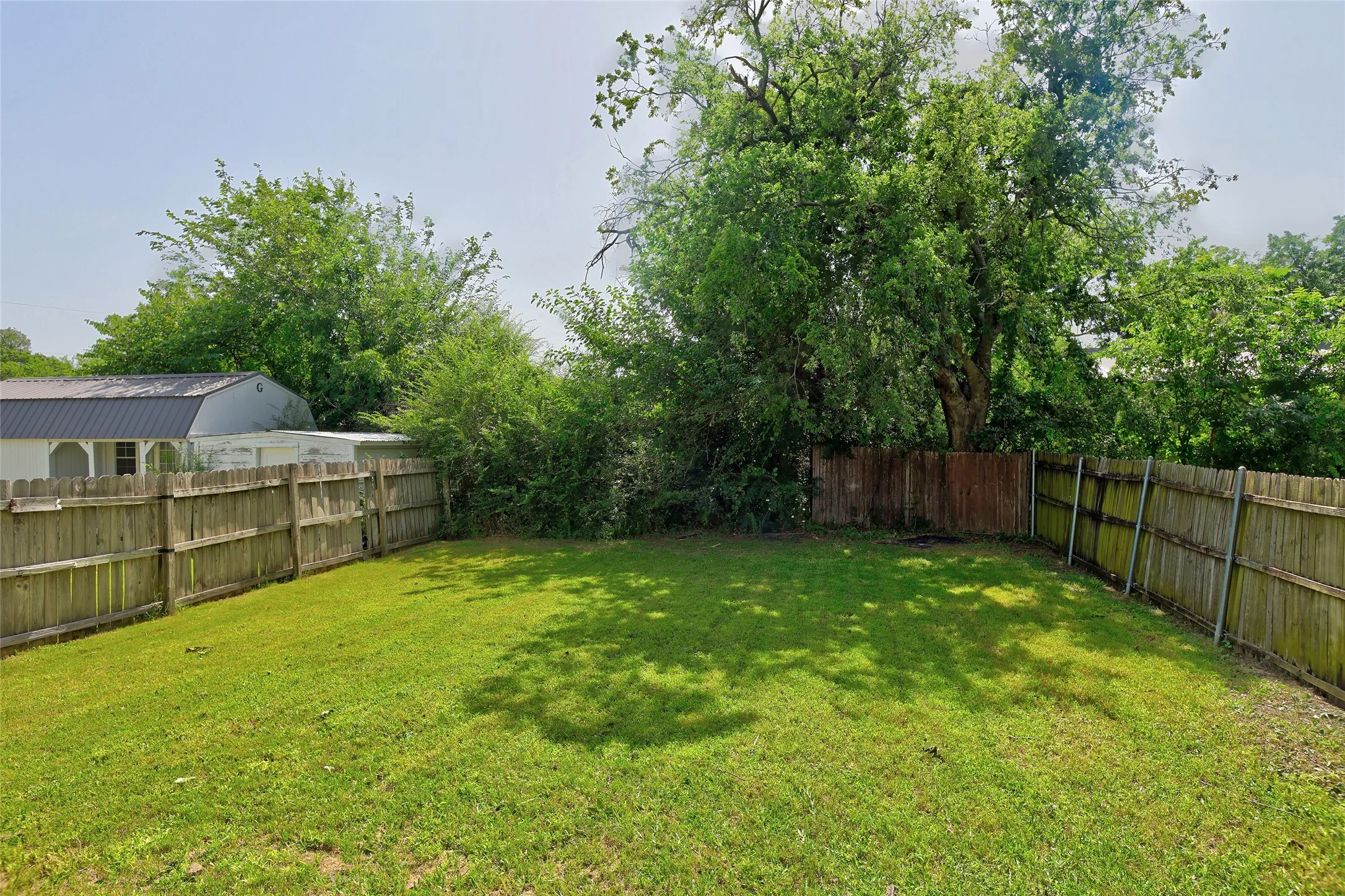 Expansive fenced backyard with established perimeter trees and green lawn space