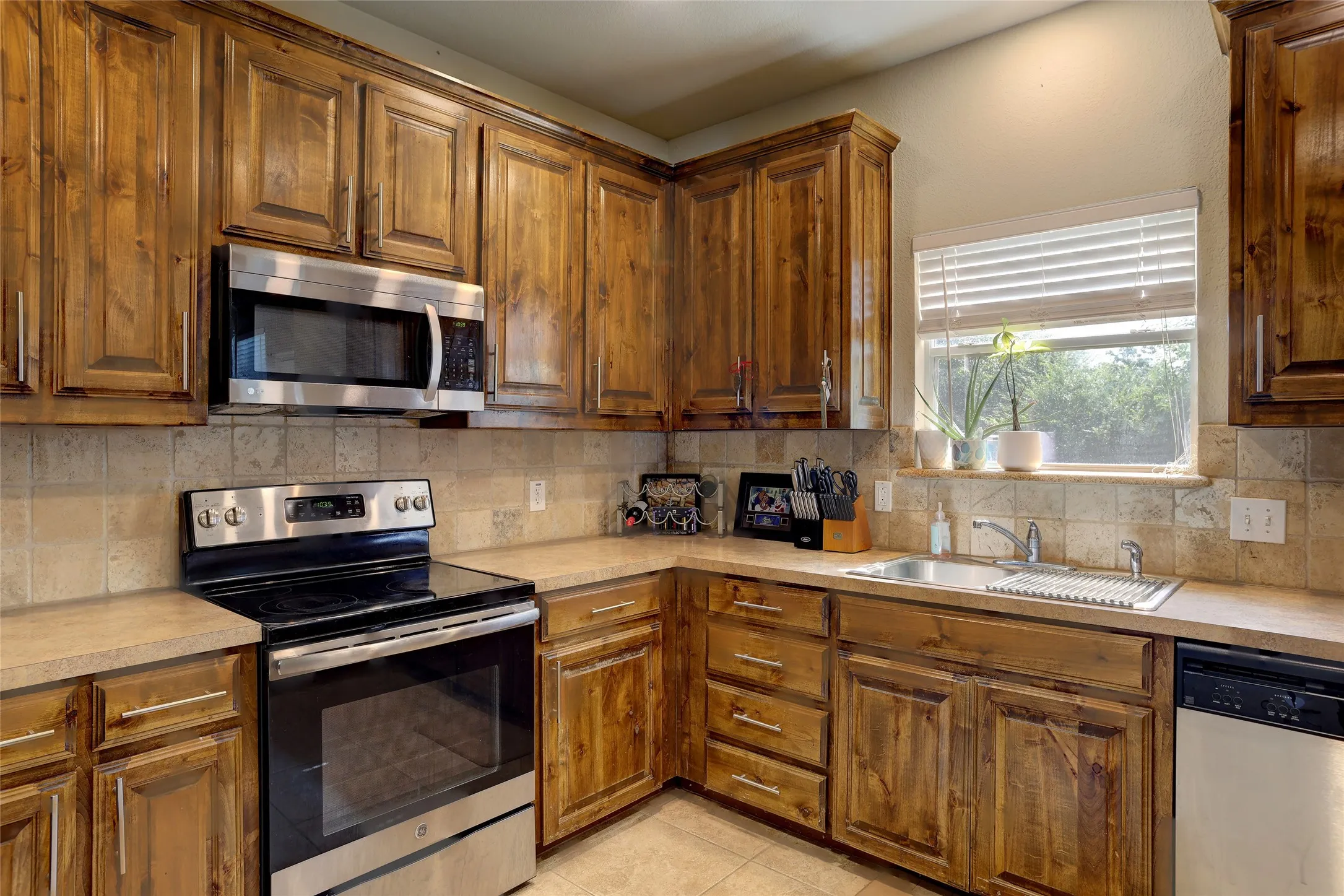 Kitchen featuring wood cabinetry, stainless steel appliances, a tile backsplash, and light-colored countertops