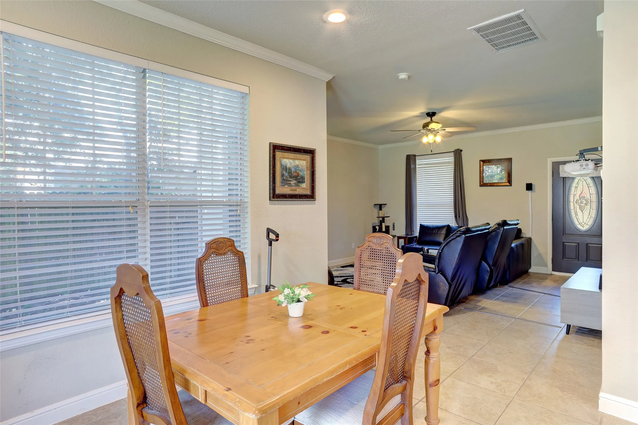 Dining area featuring a light wood-finish table, crown molding, two large windows with blinds, and tile flooring