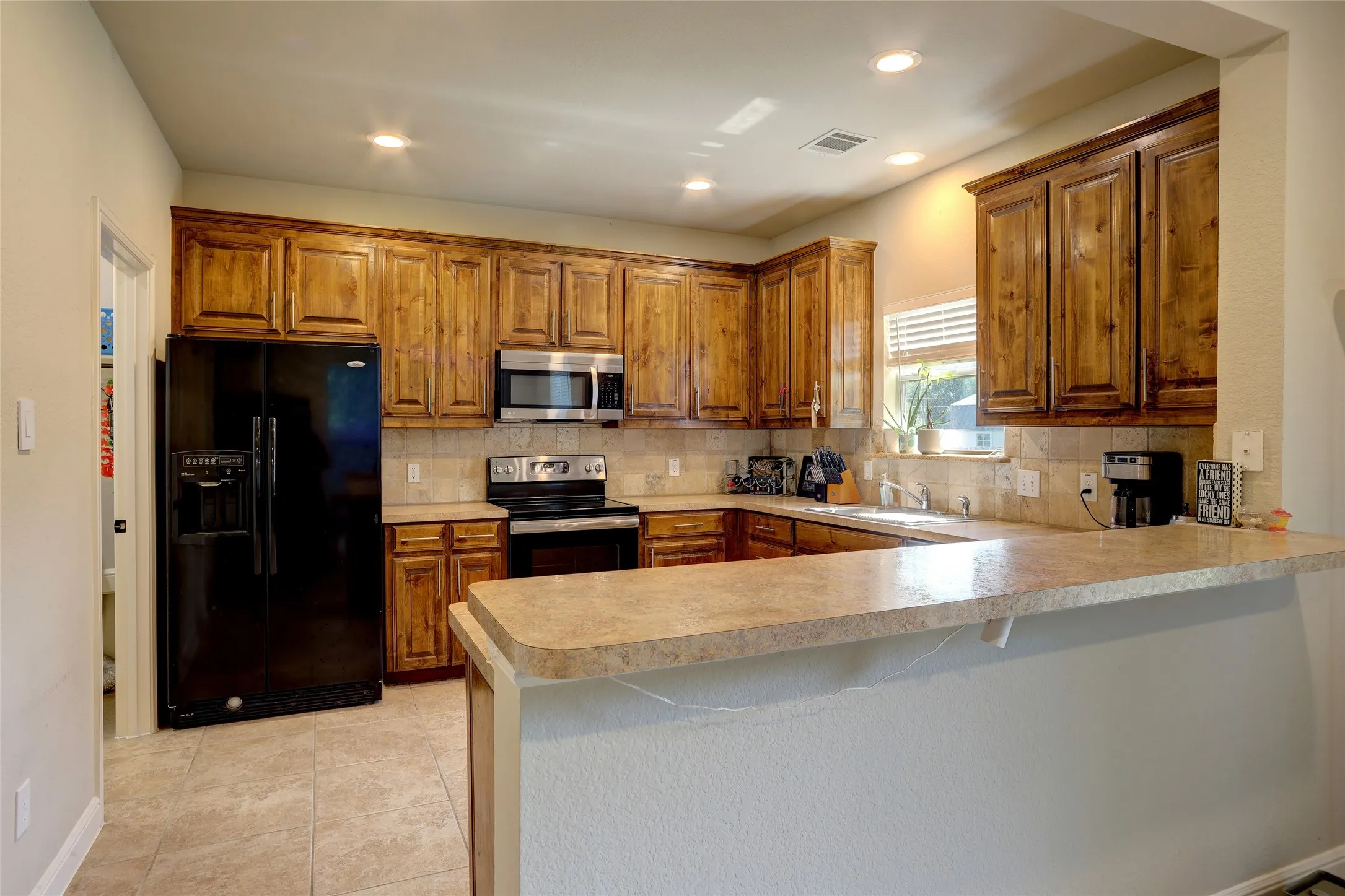 Kitchen featuring wood cabinetry, stone-look countertops, tiled backsplash, and recessed lighting