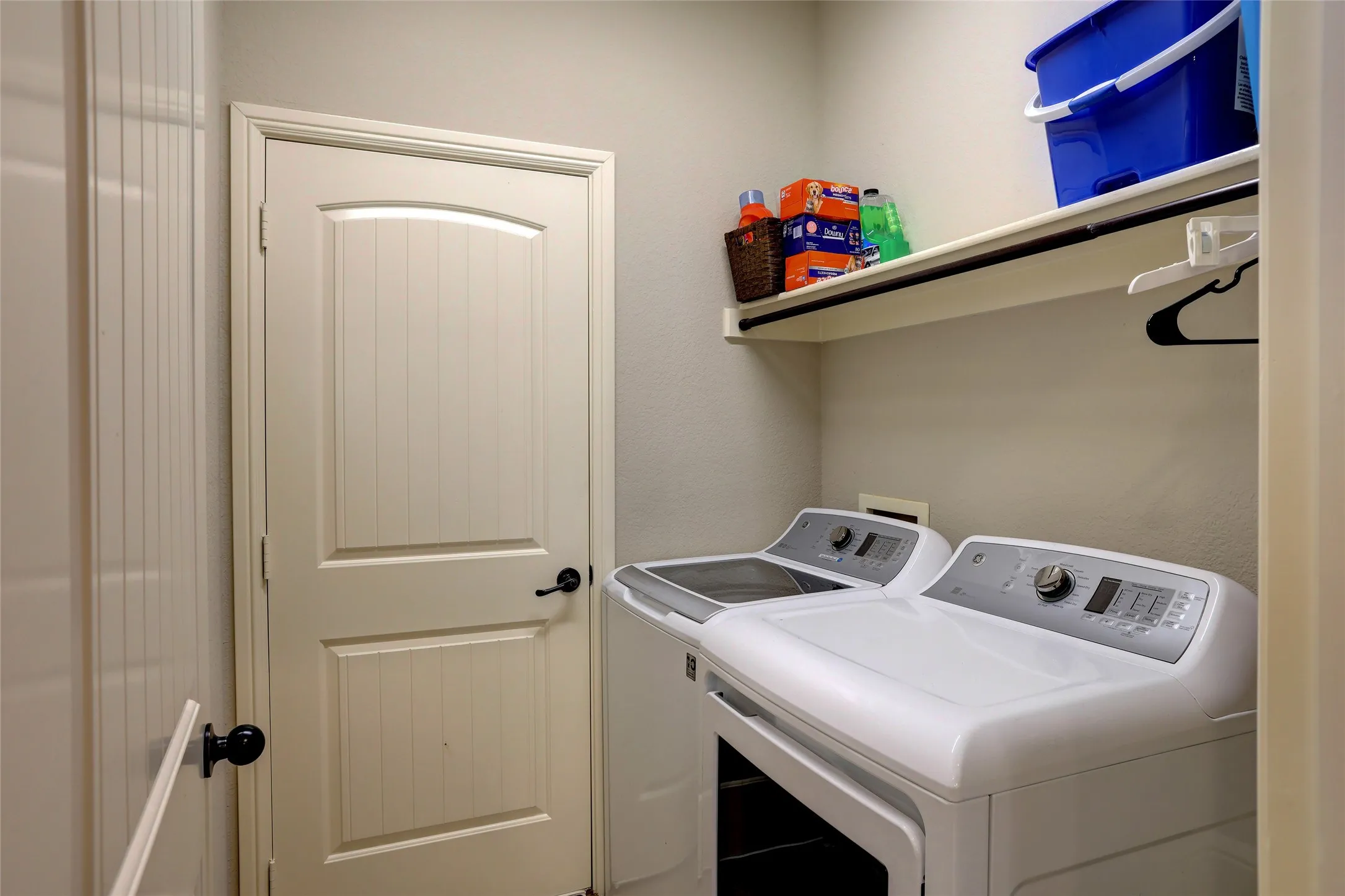Dedicated laundry area featuring a shelf with an integrated hanging rod, and beadboard-style interior door