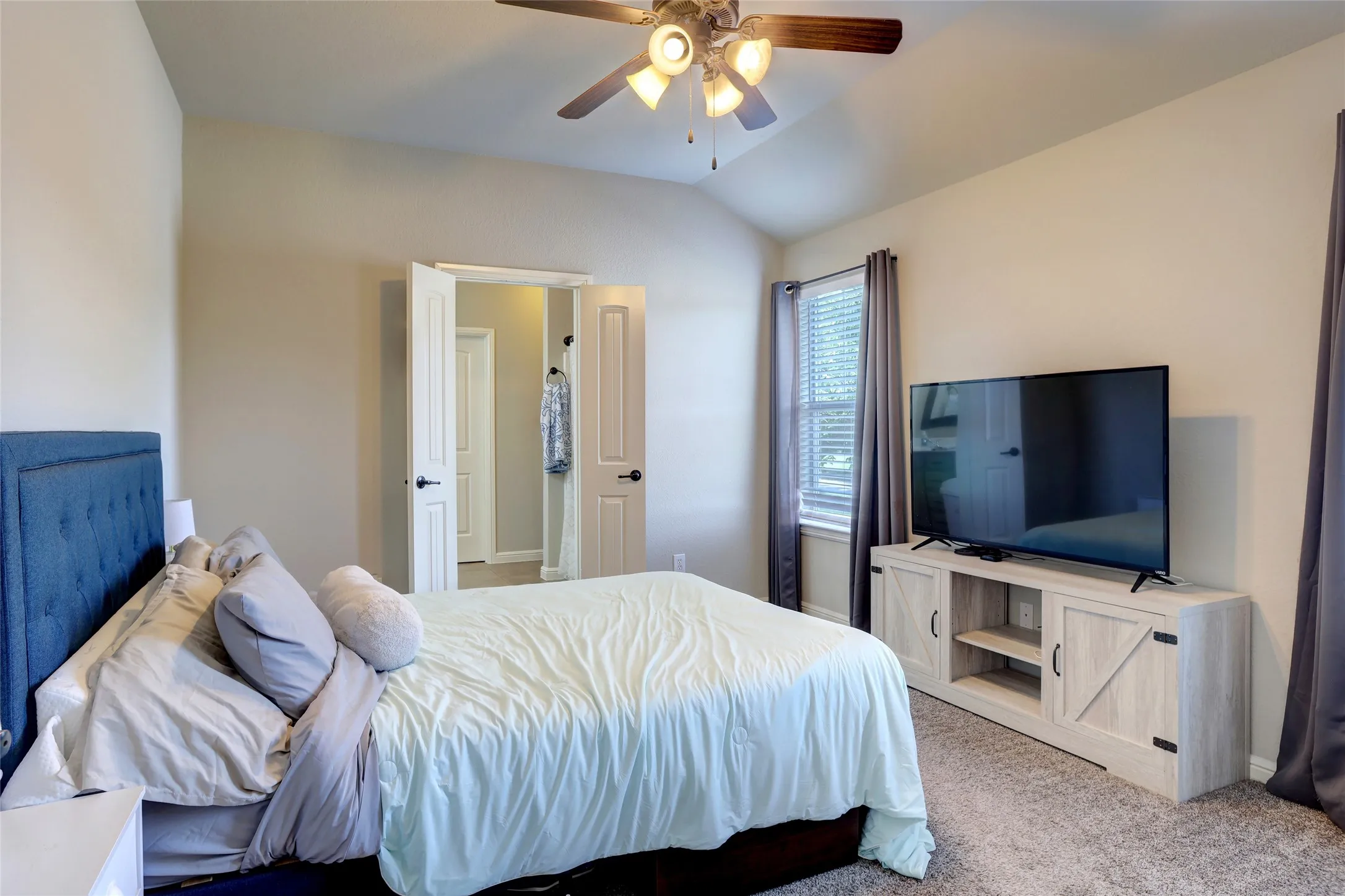 Carpeted interior space featuring a ceiling fan, vaulted ceiling, and a window with blinds