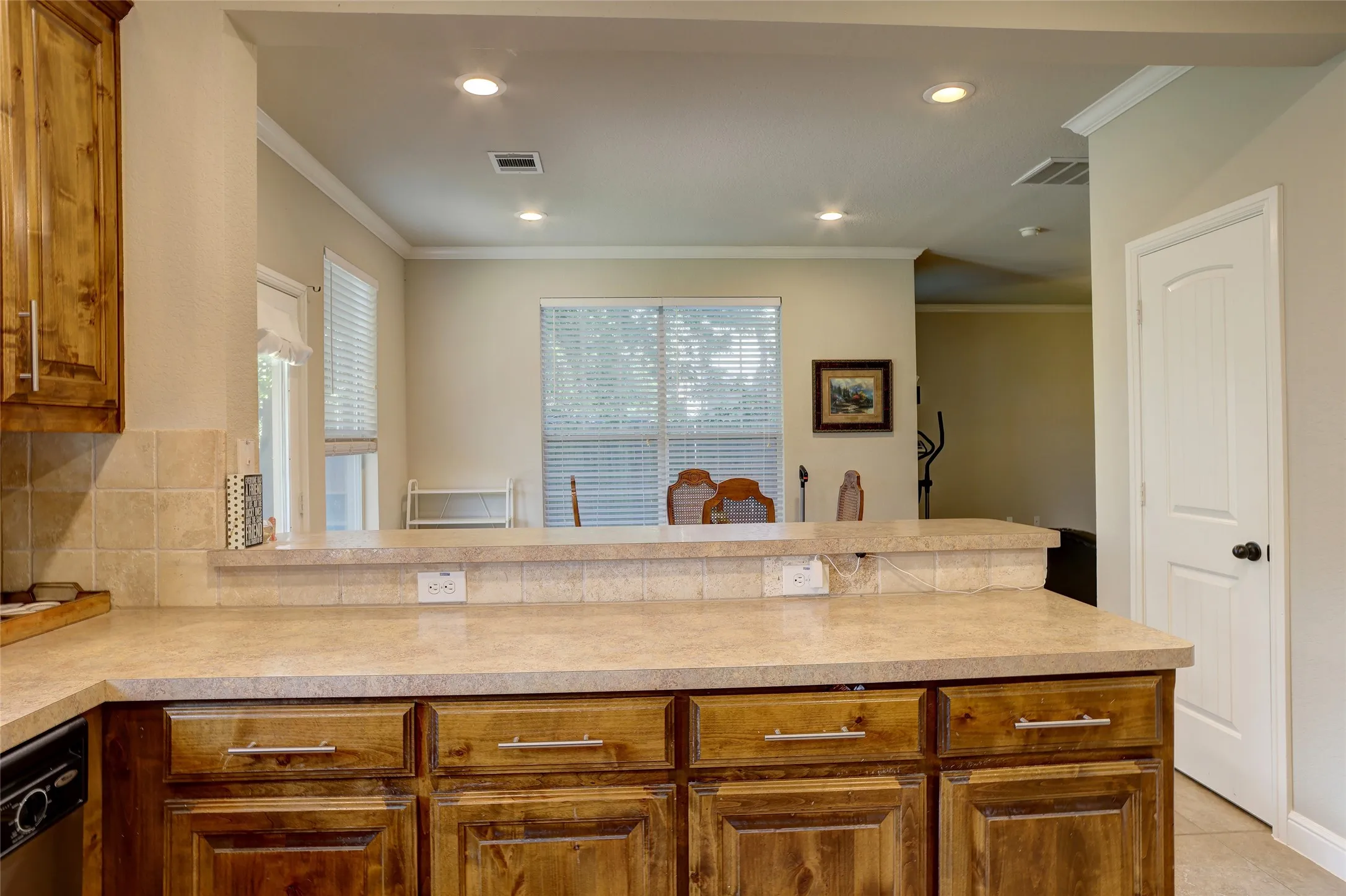 Kitchen pass-through featuring an extended countertop bar with power outlets, a tile backsplash, and wood-finish cabinetry