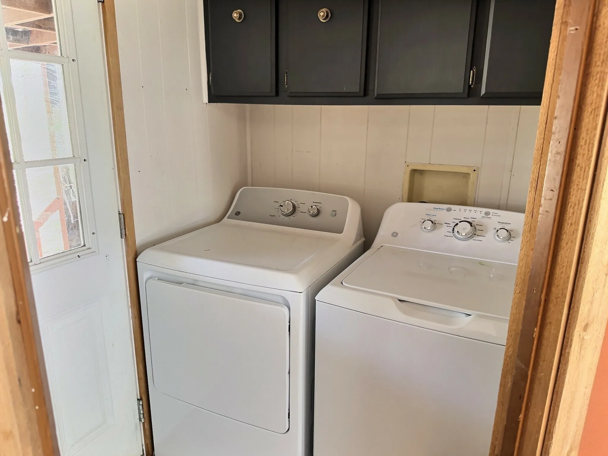 Dedicated laundry area featuring white vertical paneling and overhead dark cabinetry