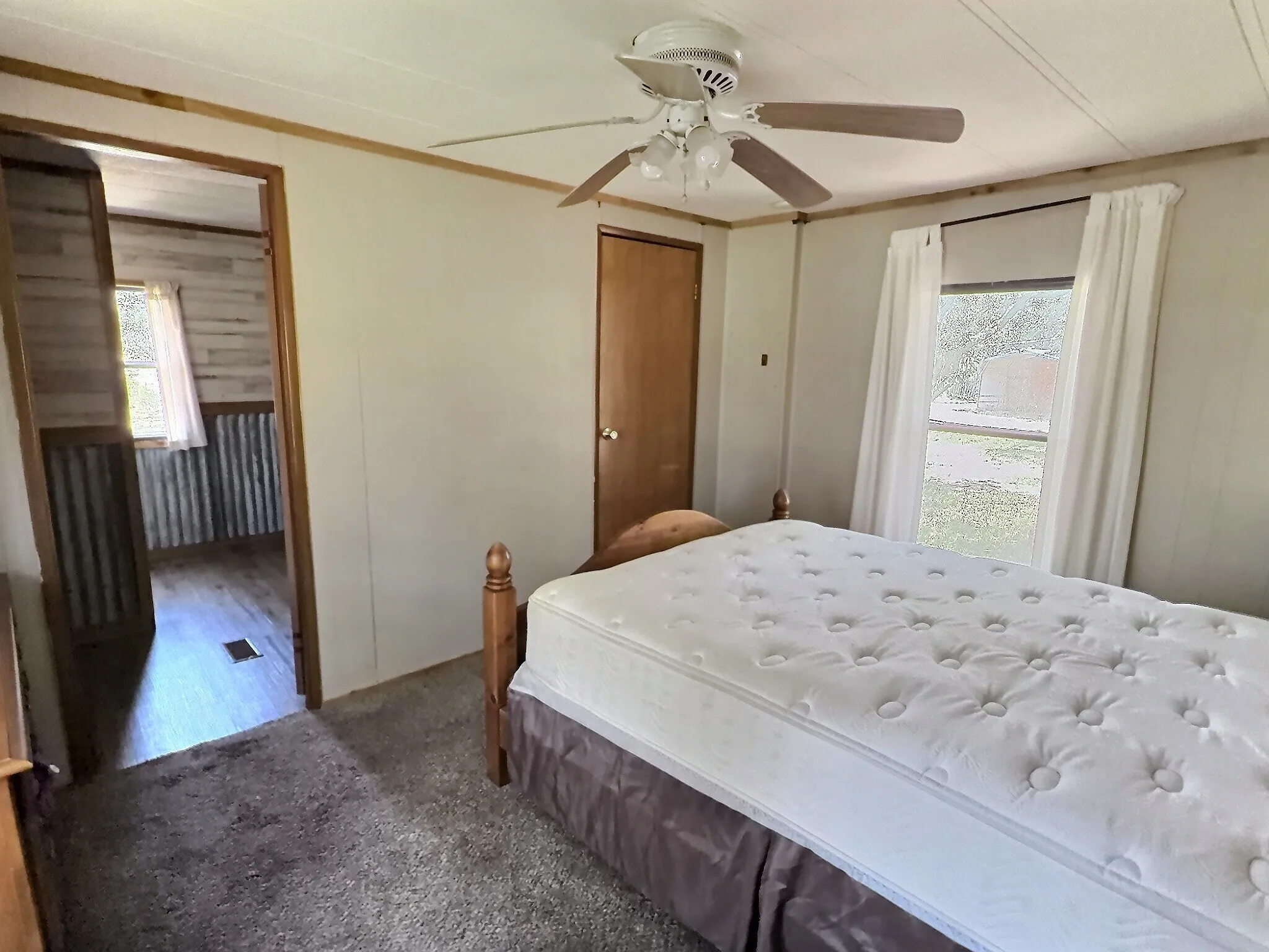 Carpeted bedroom featuring a ceiling fan with integrated lighting, a window with roller shade and curtains, and a wood-panel door