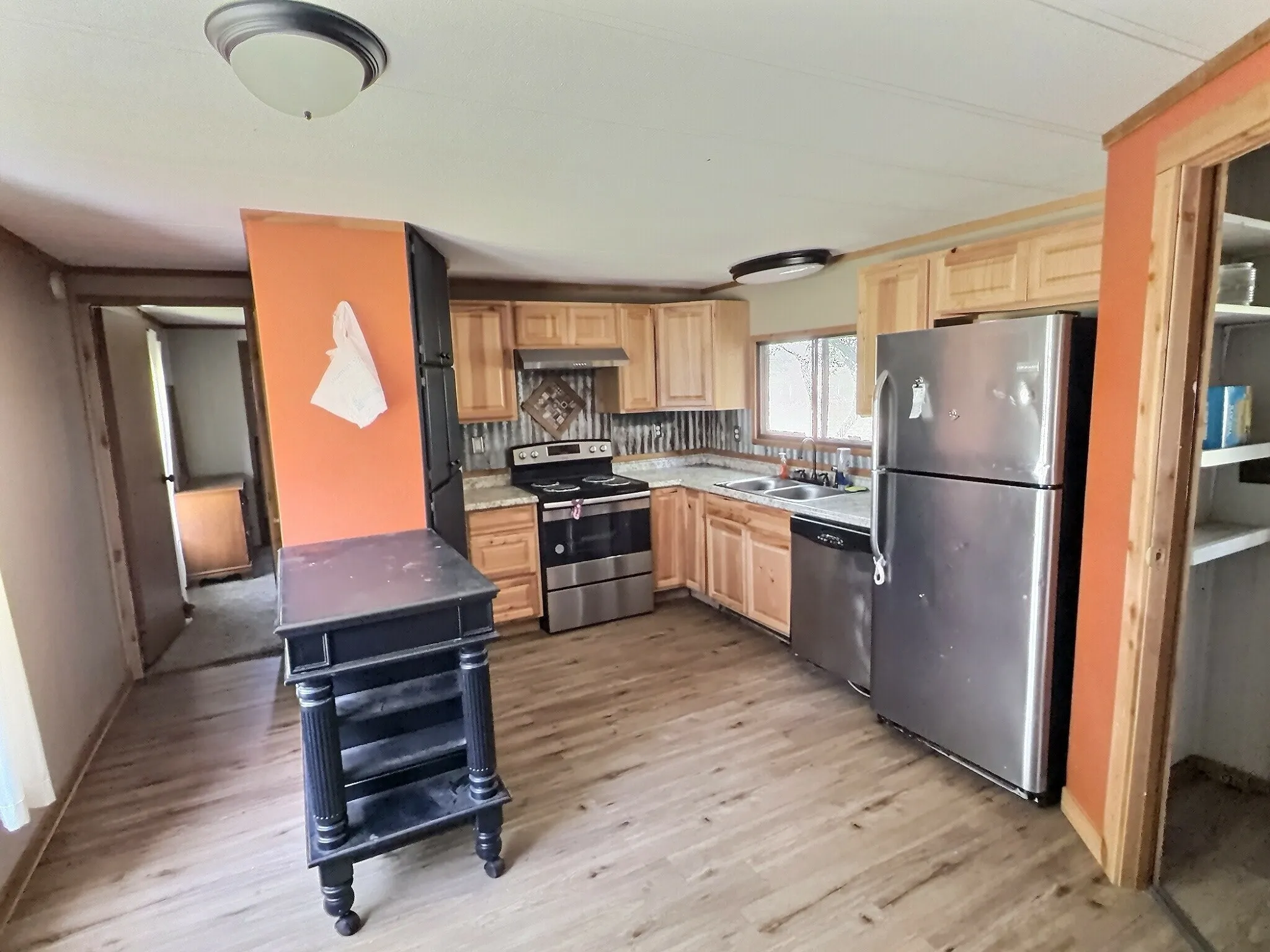 Kitchen featuring wood-finish flooring, light wood cabinetry, stainless steel appliances, and a corrugated metal backsplash