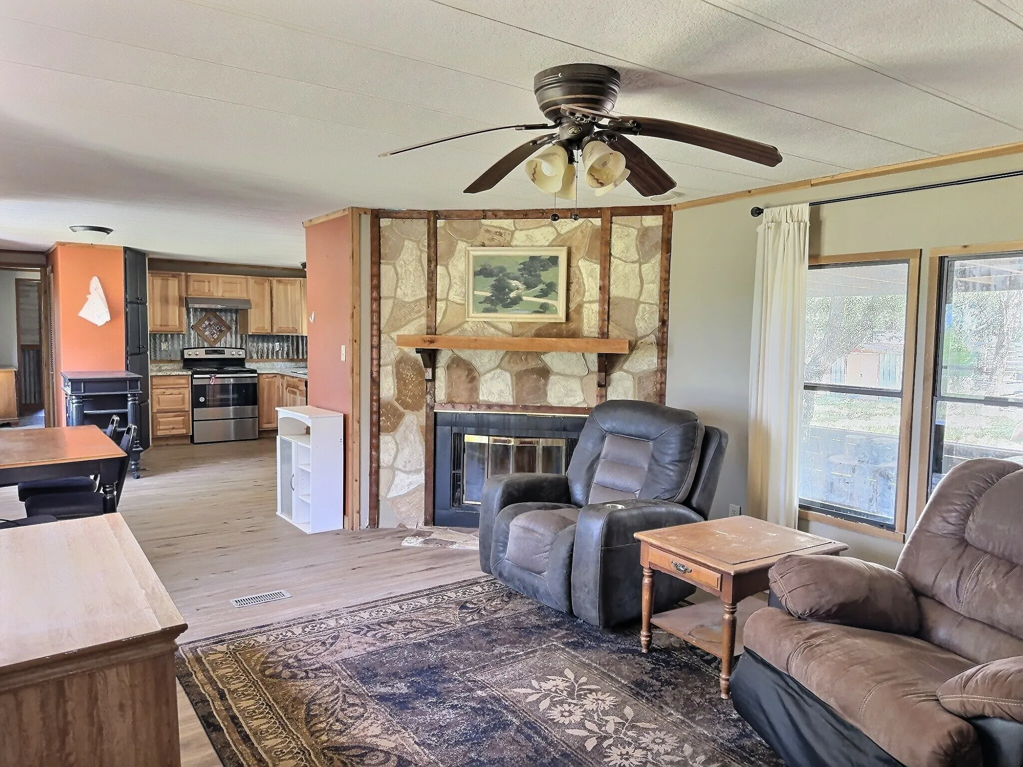 Living area featuring a stone-accented fireplace with wood mantel, ceiling fan, and wood-finish flooring