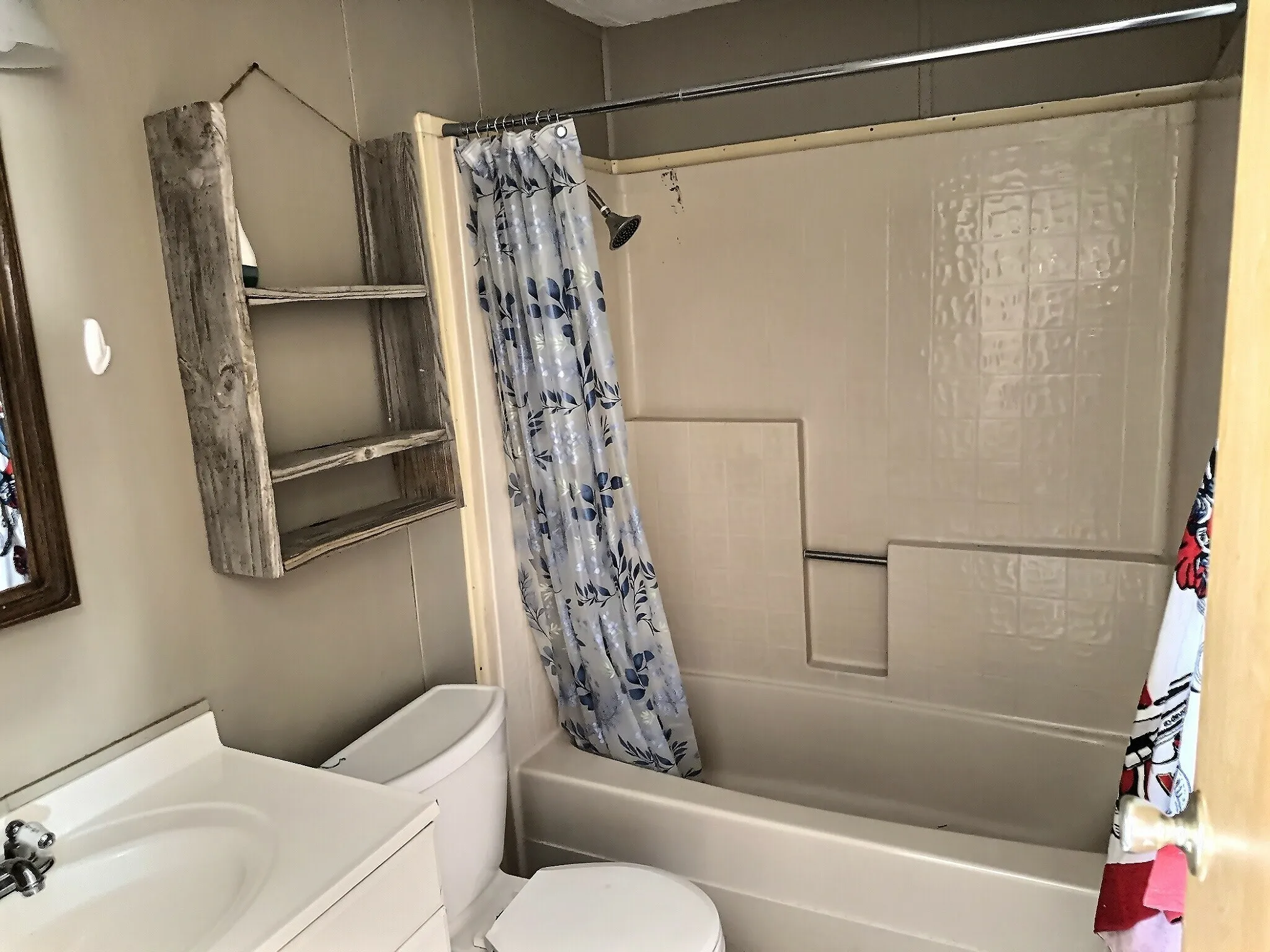 Bathroom featuring a white vanity with integrated sink, a built-in bathtub with shower, and a wall-mounted wooden shelving unit