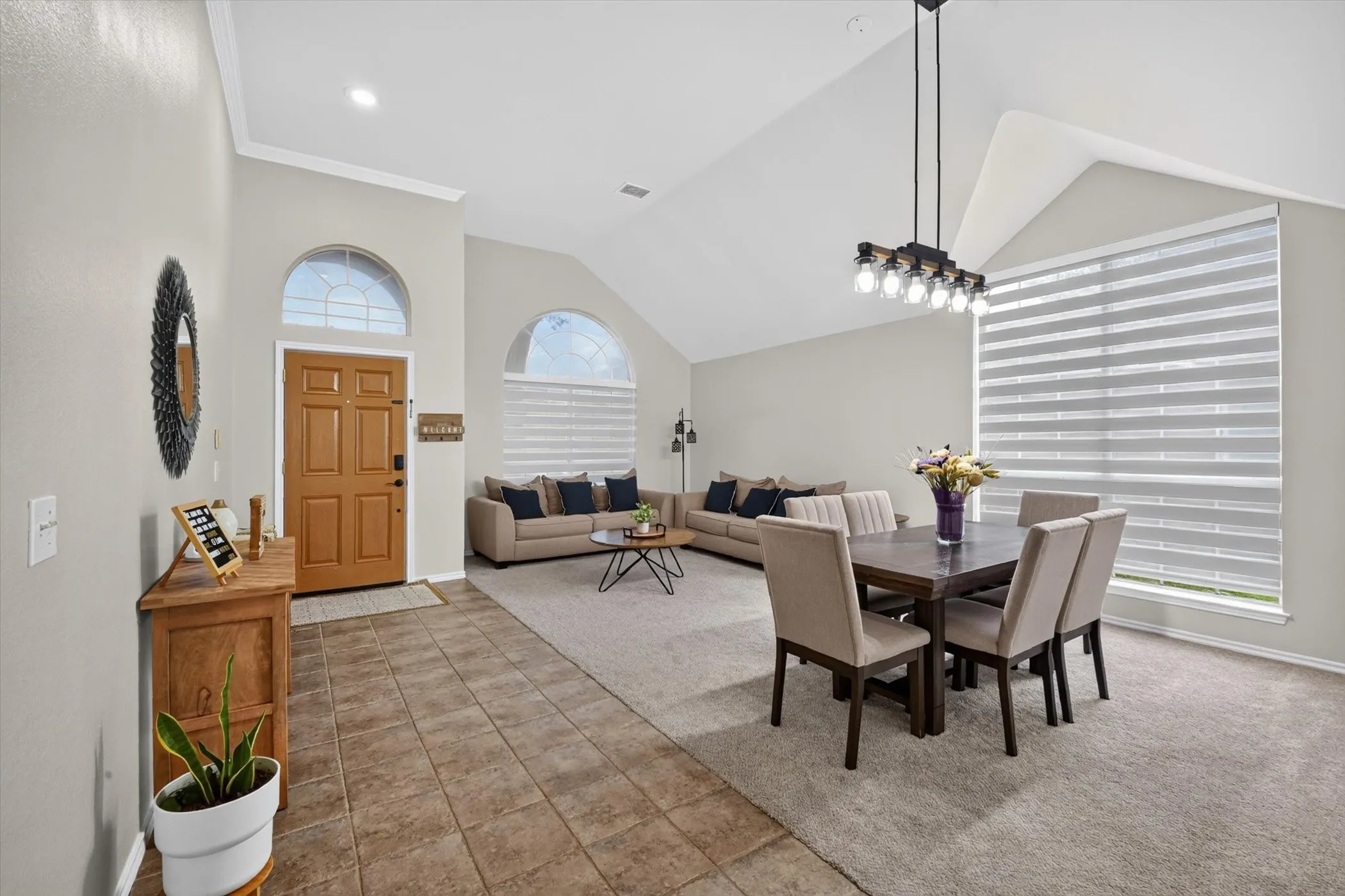 Spacious living area featuring vaulted ceilings, a prominent decorative light fixture, and a large window with horizontal blinds
