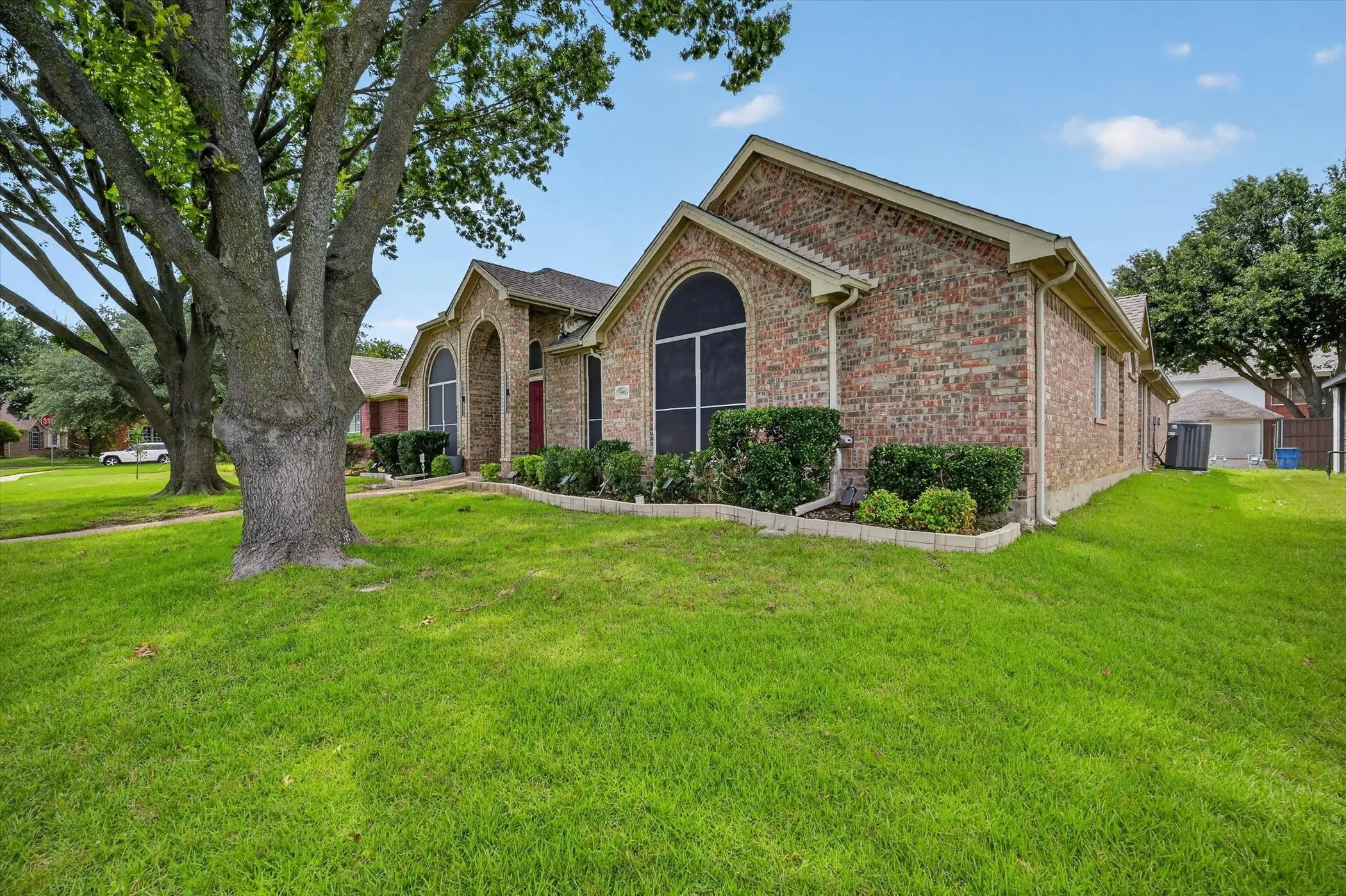 Brick exterior with arched windows featuring dark screens, a red front door, and a landscaped foundation
