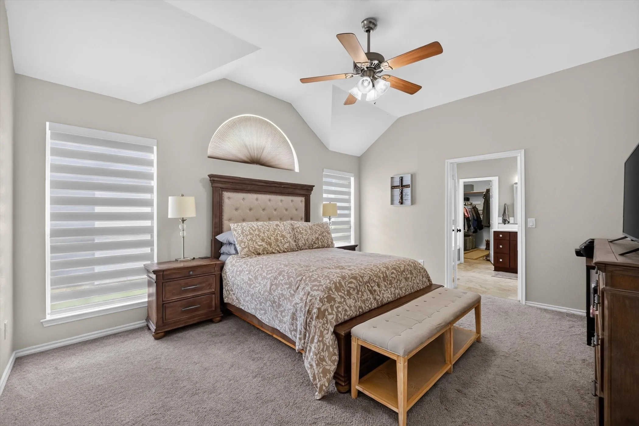 Carpeted room featuring a vaulted ceiling with a ceiling fan, a decorative arched window, and two rectangular windows with horizontal blinds