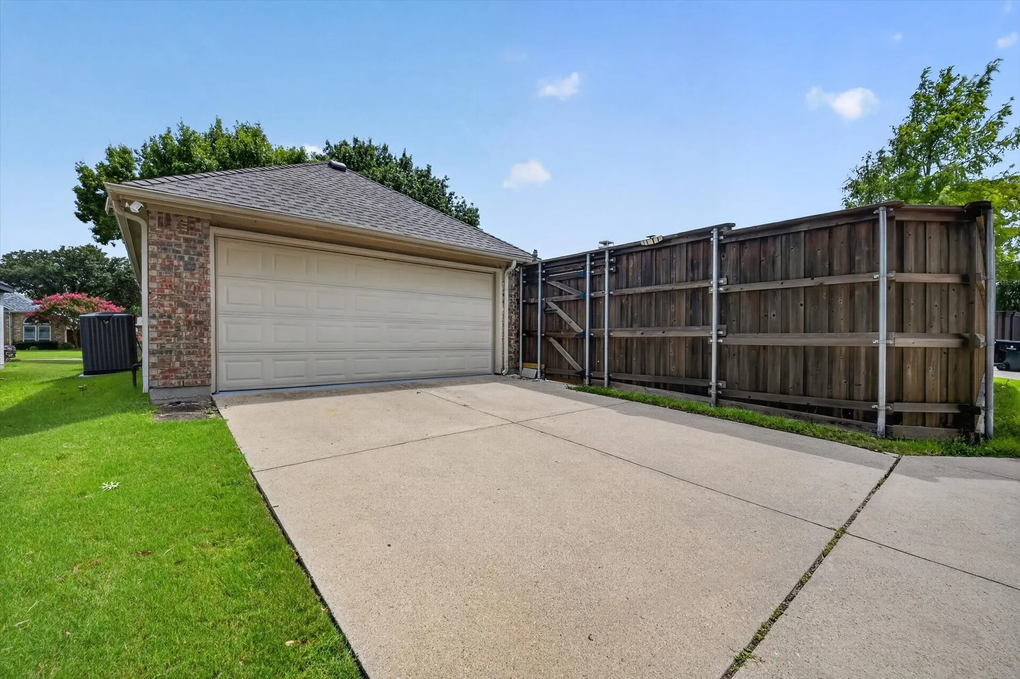 Attached garage with a tan panel door, brick siding, and a shingled roof