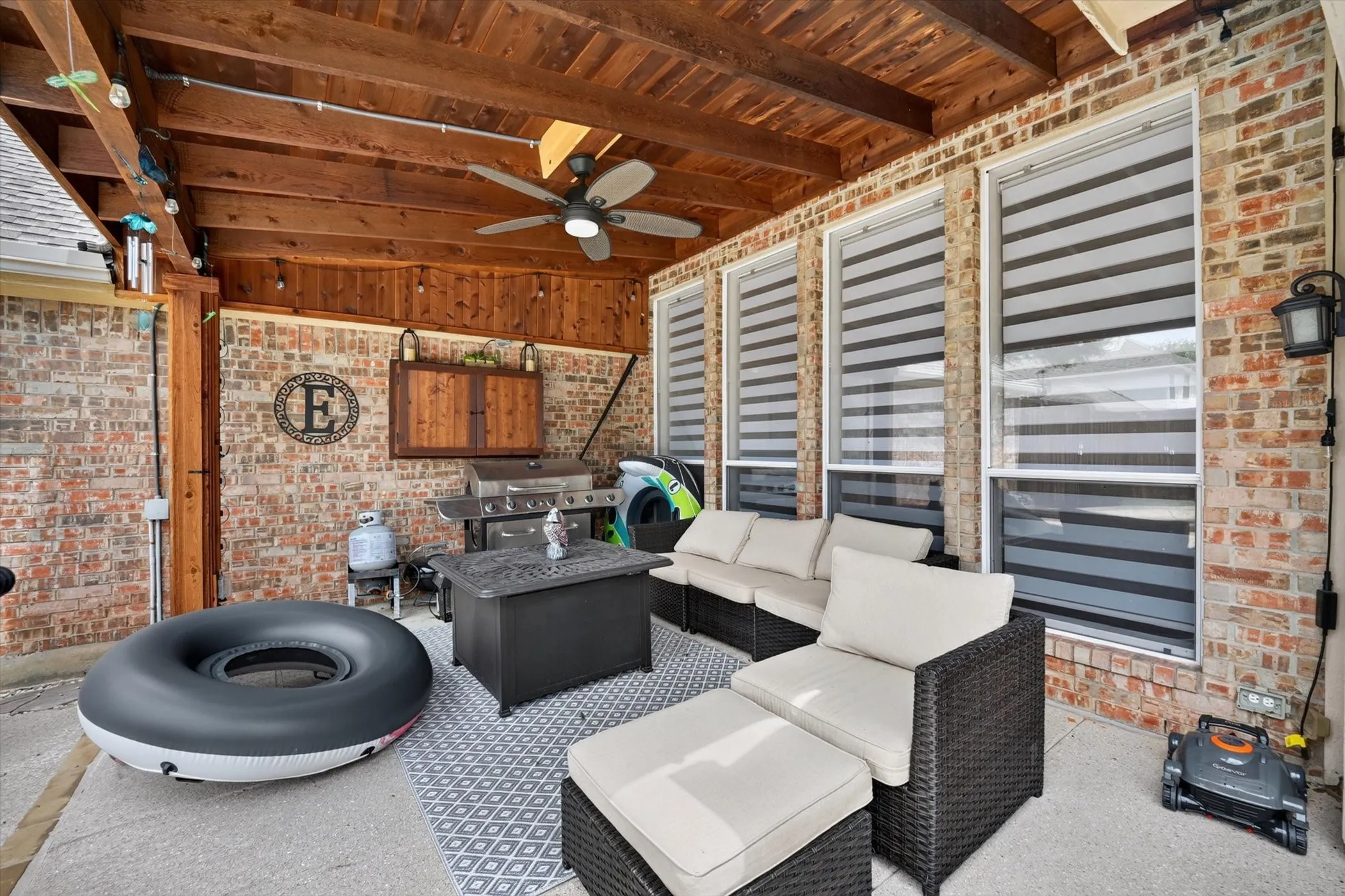 Covered patio featuring an exposed wood beam ceiling, brick exterior, and multiple windows with horizontal blinds