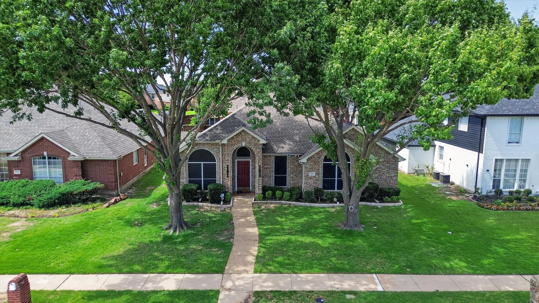 Brick exterior with a prominent red front door, flanked by two mature deciduous trees