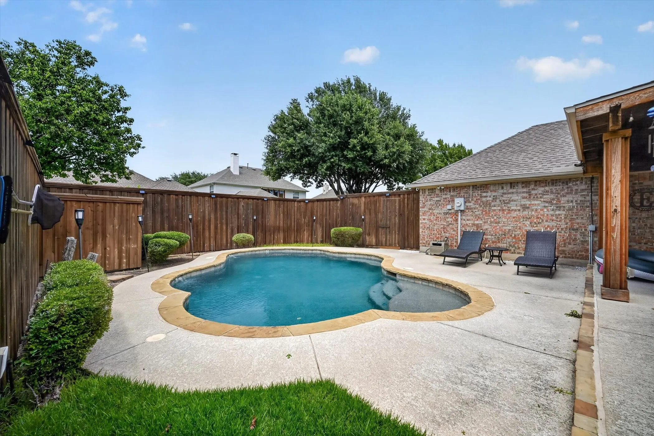 Backyard swimming pool featuring a curved concrete patio, a privacy fence, and brick exterior architecture