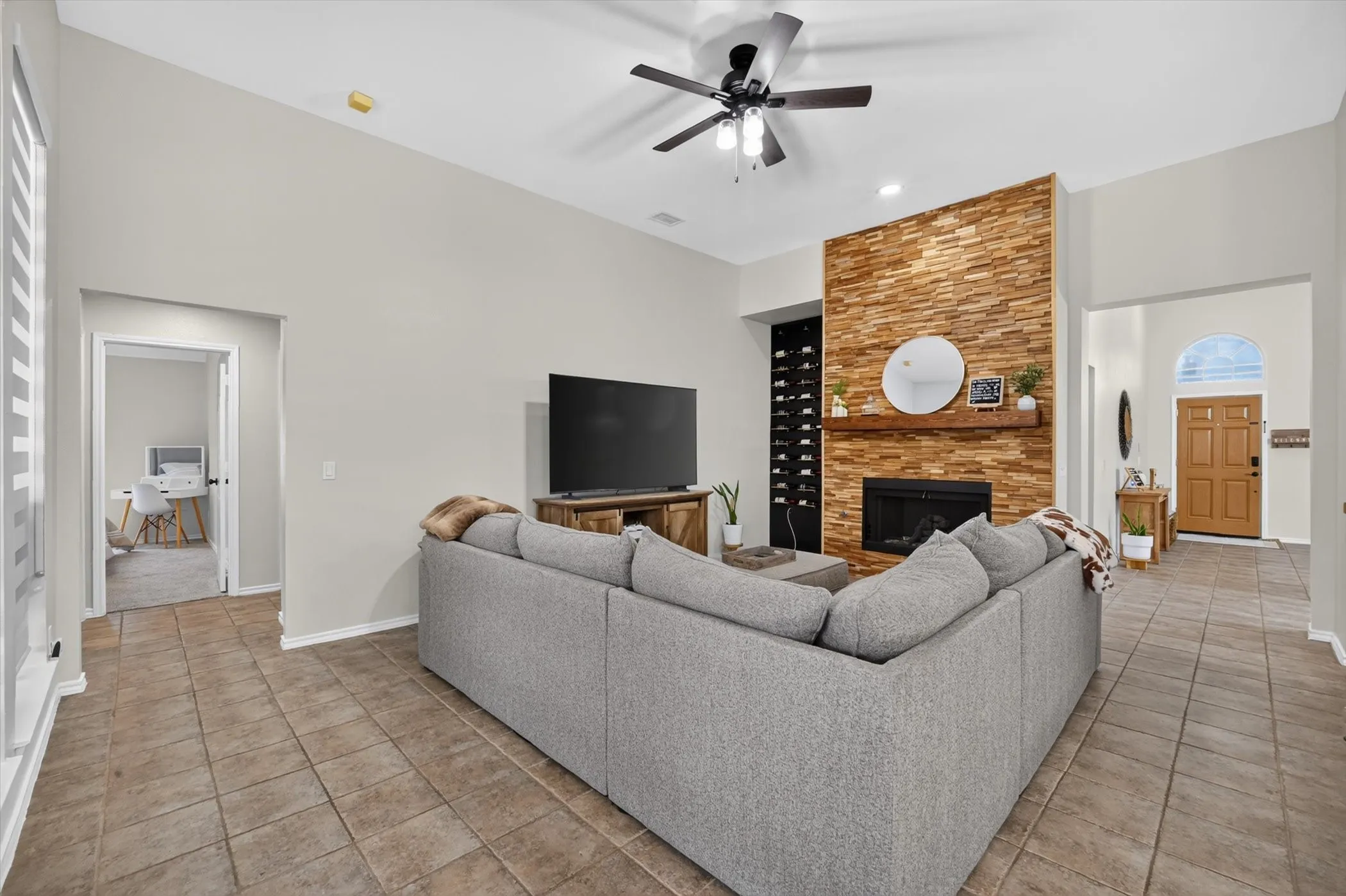 Living area featuring a floor-to-ceiling stacked stone fireplace with a wood mantle, vaulted ceilings, a ceiling fan, and tile flooring