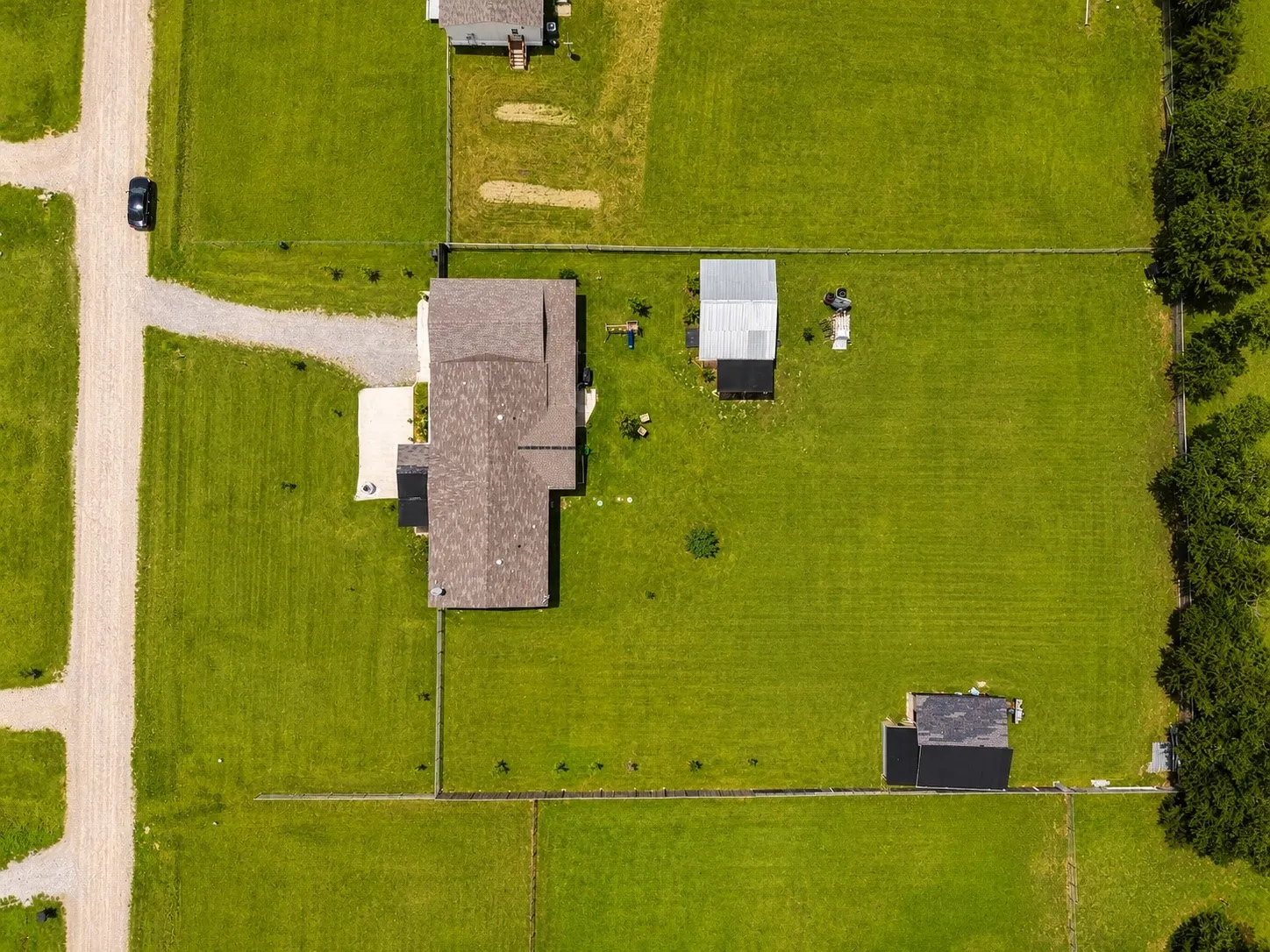 Spacious property featuring a main residence with a gabled roof, two outbuildings, extensive green lawn, and a light-colored gravel driveway