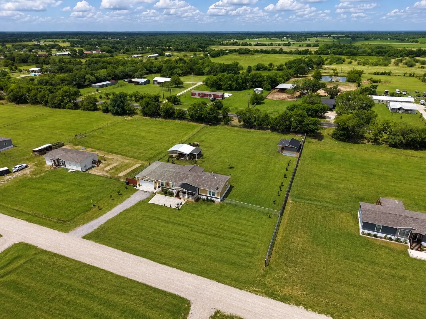 Aerial perspective showcasing a single-family residence with a light-colored exterior and a dark roof, situated on a substantial green lot